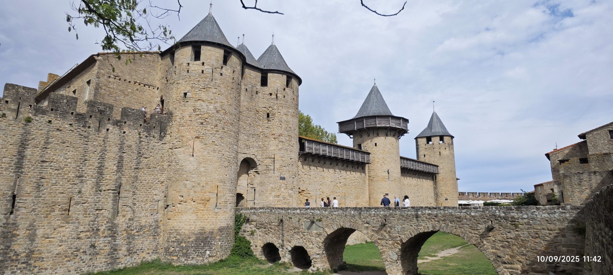 Imponente castillo medieval de piedra con torres cónicas y un puente de arcos.