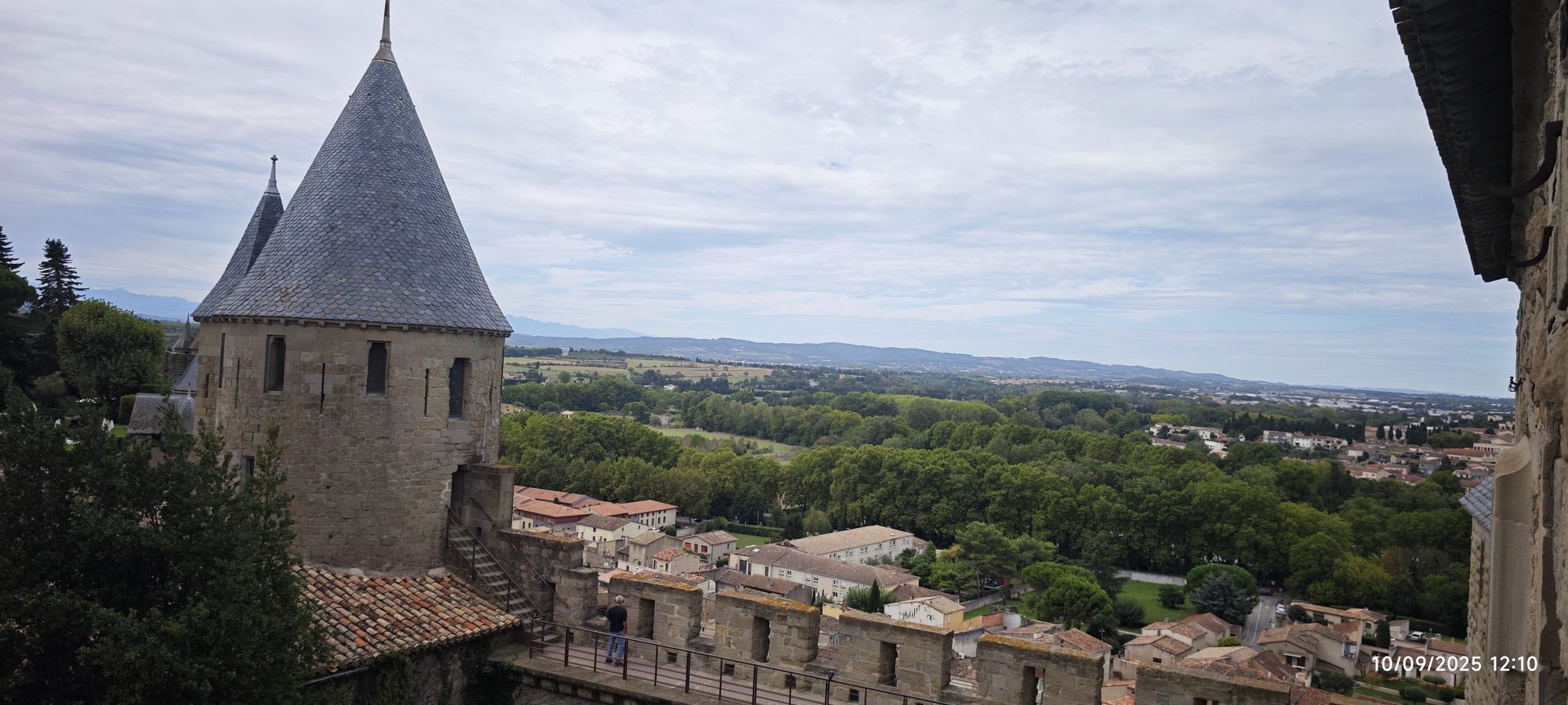 Torre cónica de piedra y murallas medievales con vistas al valle verde de Carcasona.