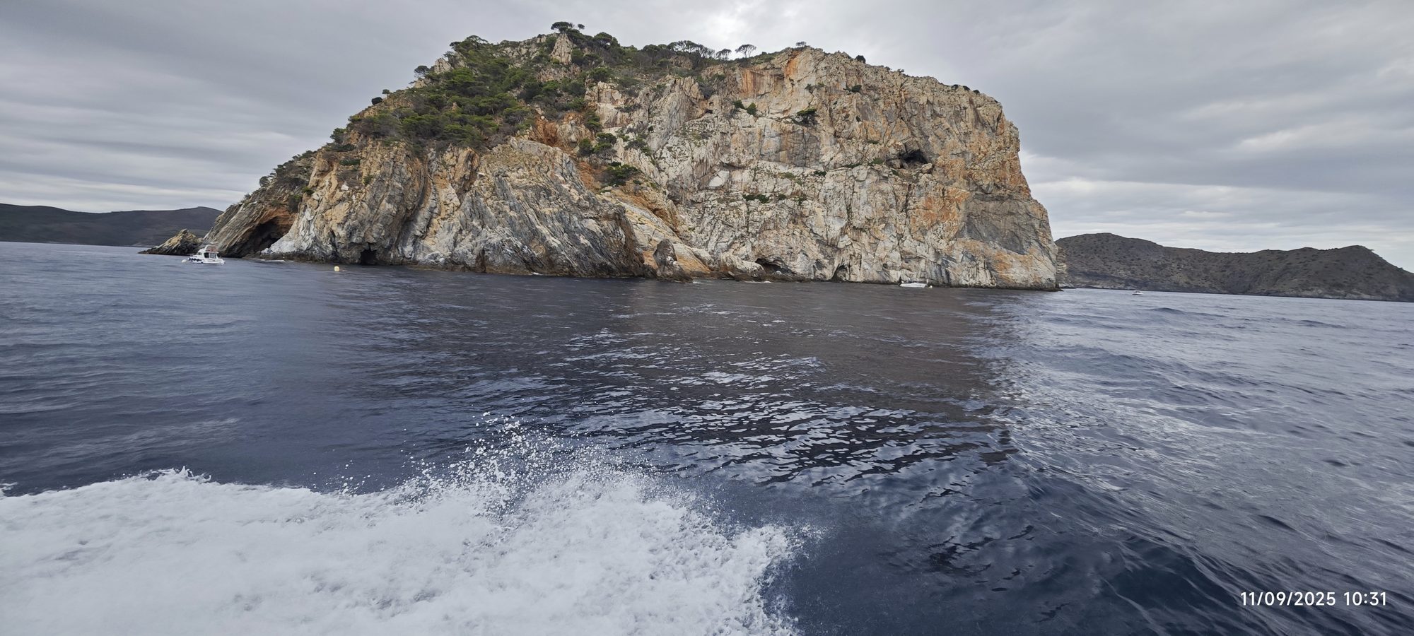 Acantilados rocosos emergiendo del mar Mediterráneo vistos desde la estela de un barco.