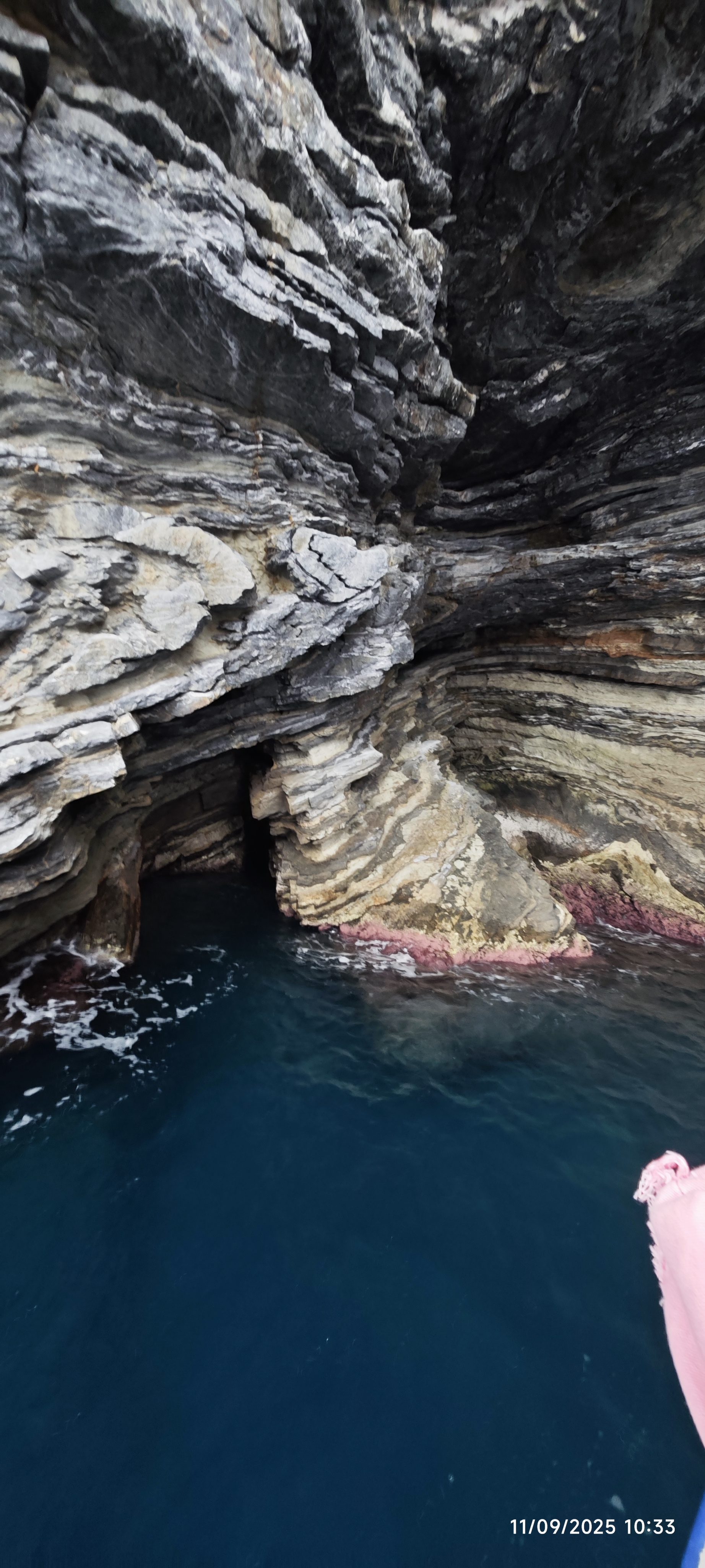 Cueva marina y acantilado rocoso con estratos de piedra sobre agua azul en Begur.