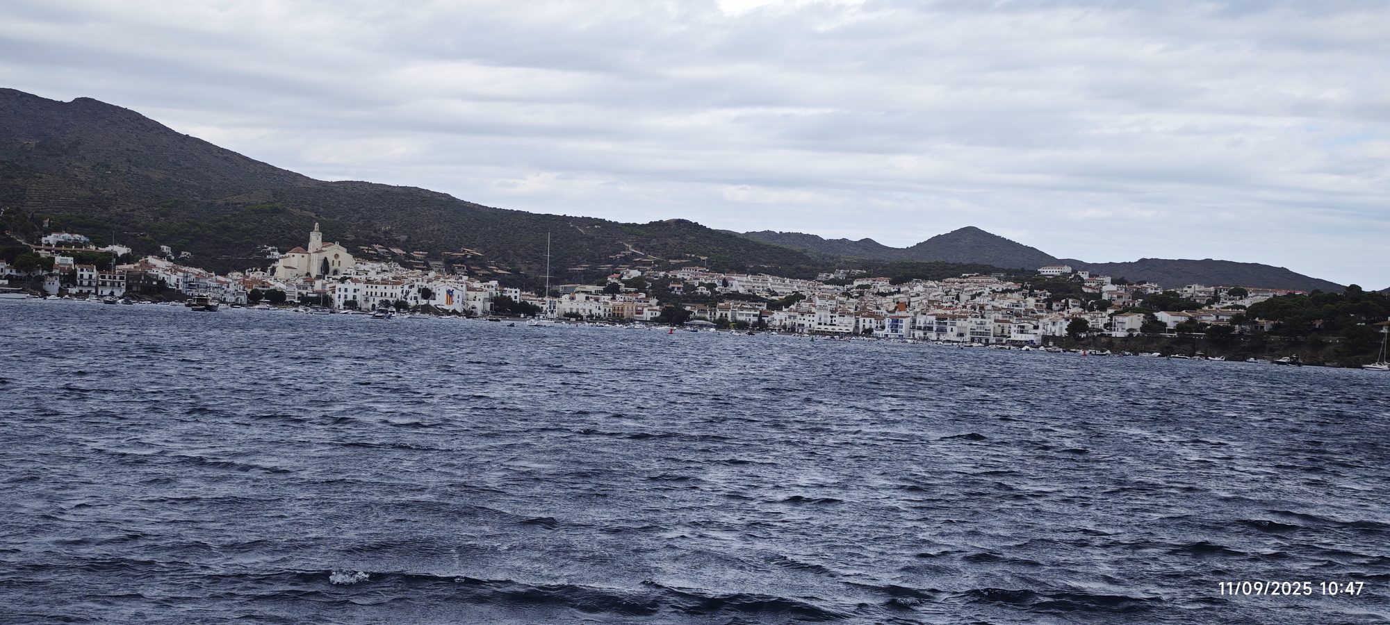 Casas blancas de Cadaqués junto al mar agitado bajo un cielo nublado.