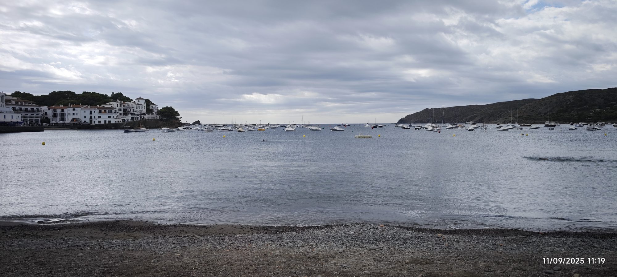 Casas blancas y barcos fondeados en la bahía de Cadaqués bajo un cielo nublado.