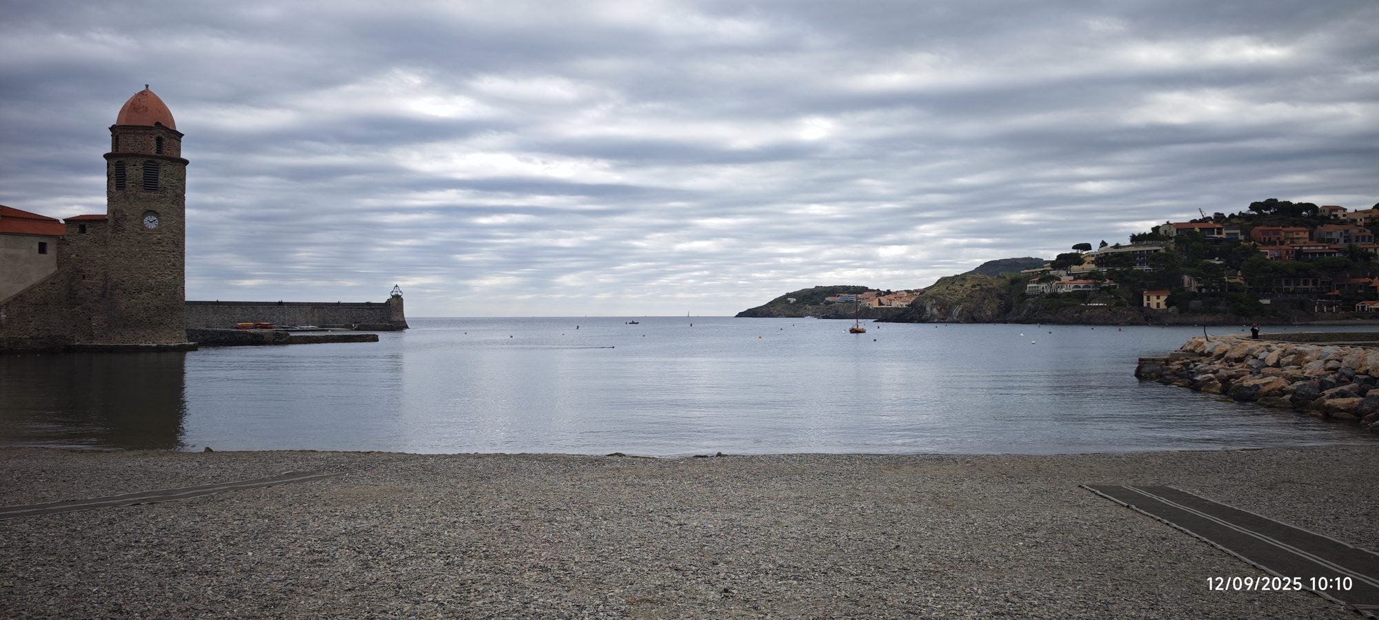 Iglesia con campanario junto a la bahía y playa de guijarros bajo cielo nublado.
