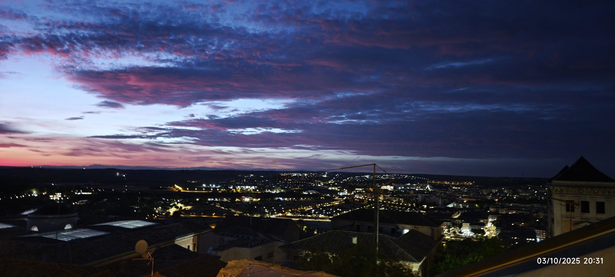 Vista panorámica del atardecer con nubes púrpuras y luces de la ciudad de Toledo.