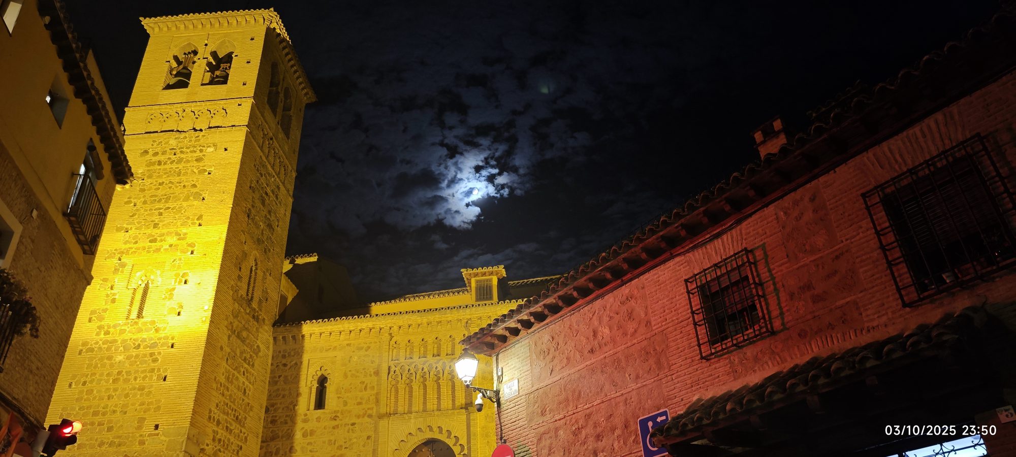 Torre de piedra iluminada y fachada histórica bajo el cielo nocturno con luna llena.