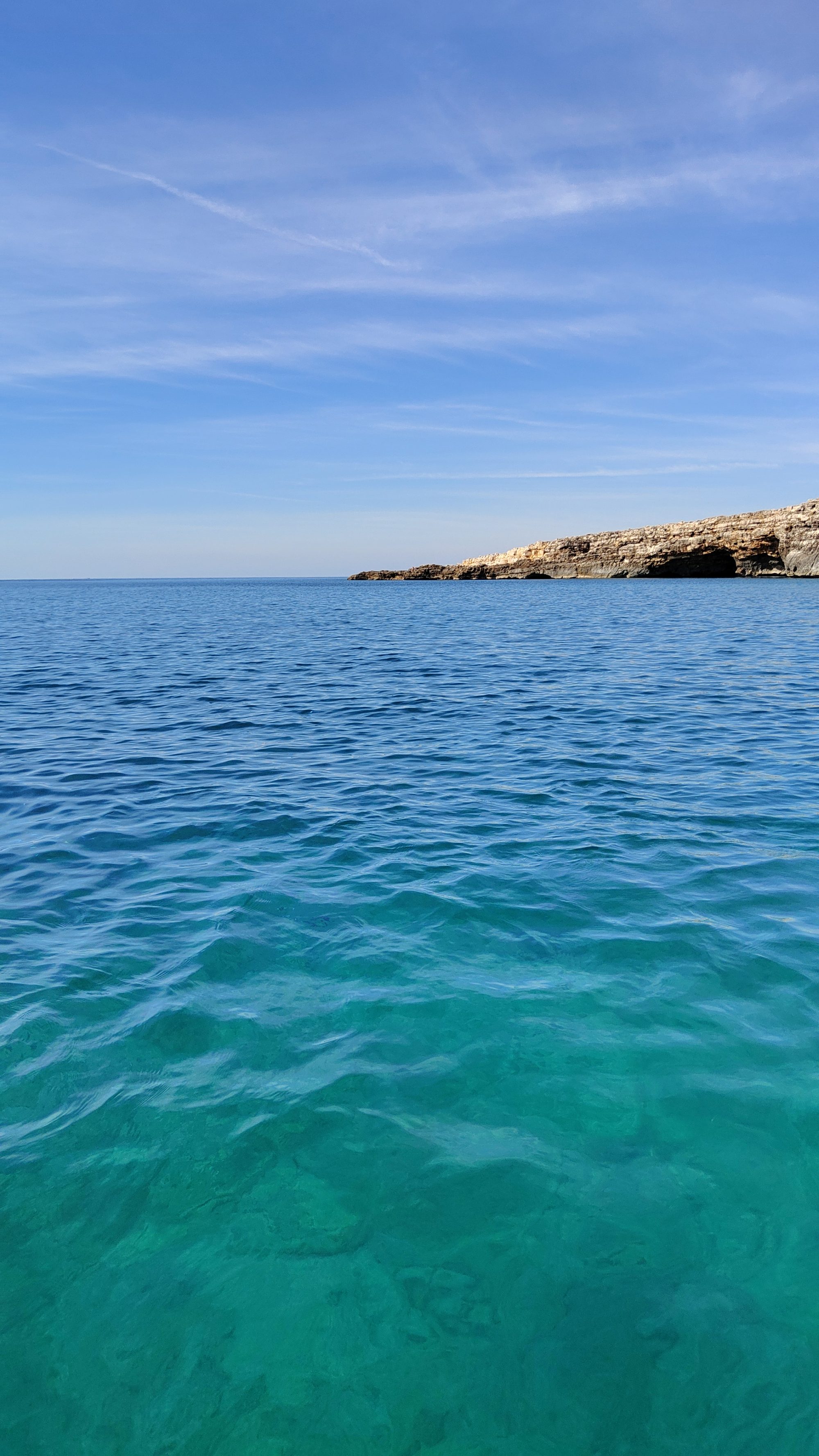 Aguas cristalinas de color turquesa frente a acantilados rocosos bajo un cielo despejado.