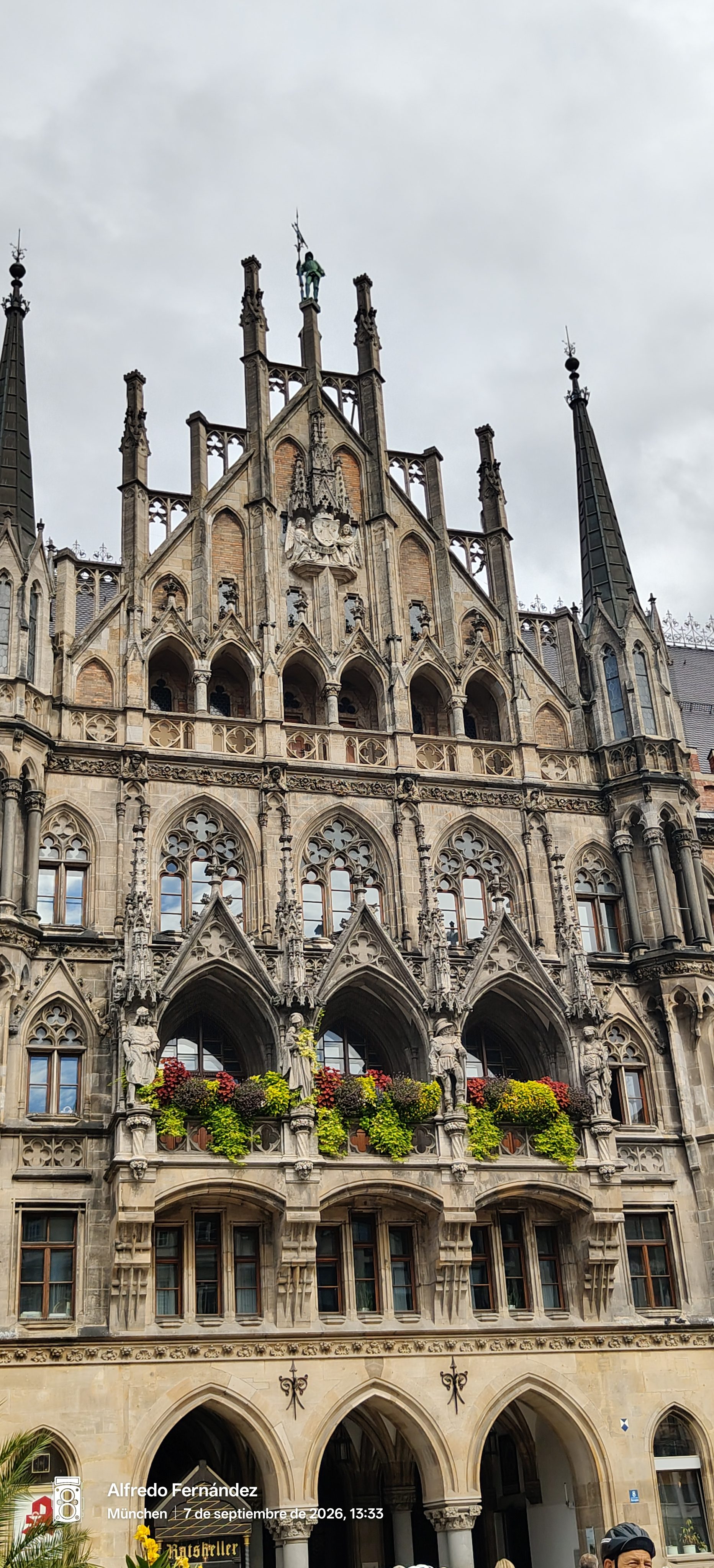 Fachada neogótica del Nuevo Ayuntamiento de Múnich con arcos ornamentados y balcones floridos.
