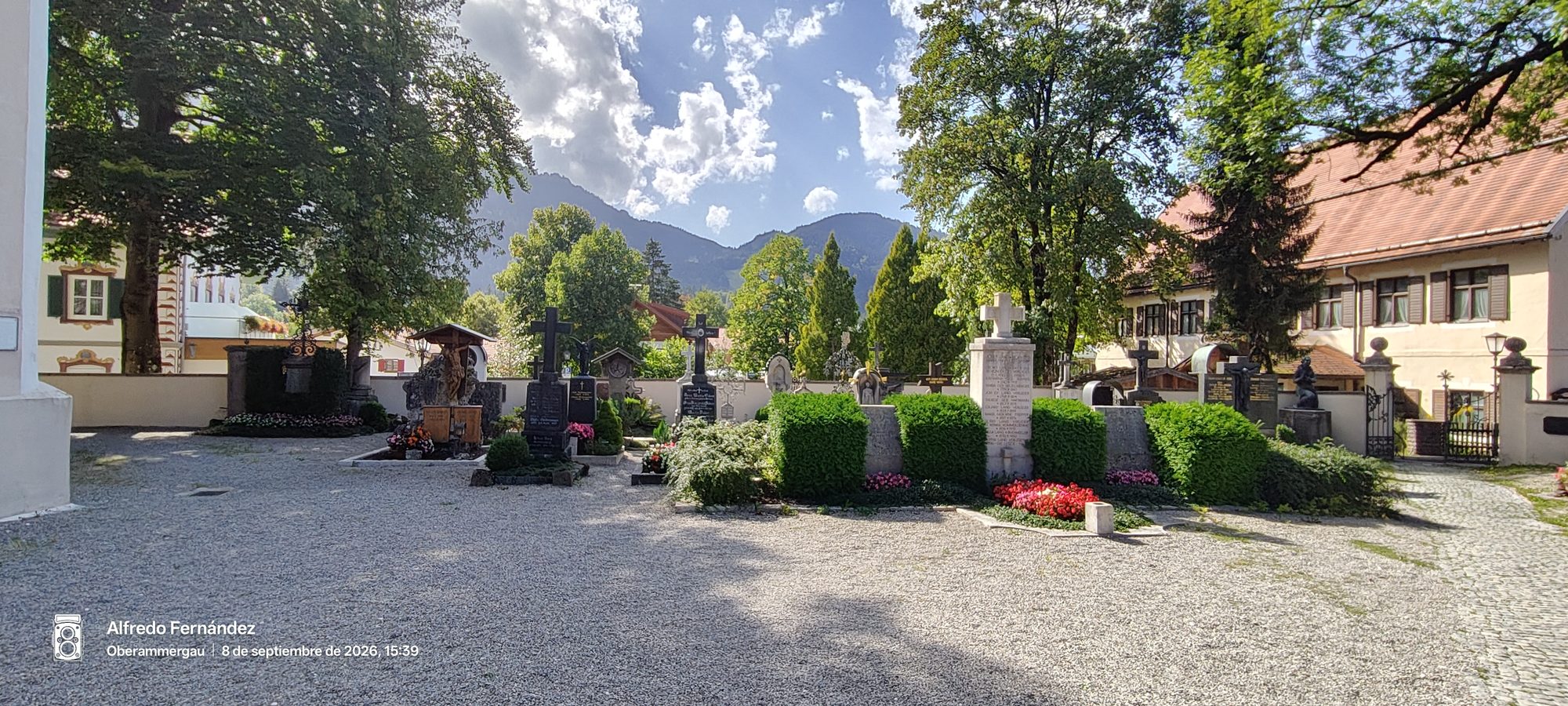 Antiguo cementerio con lápidas decoradas, setos y flores con montañas alpinas de fondo.