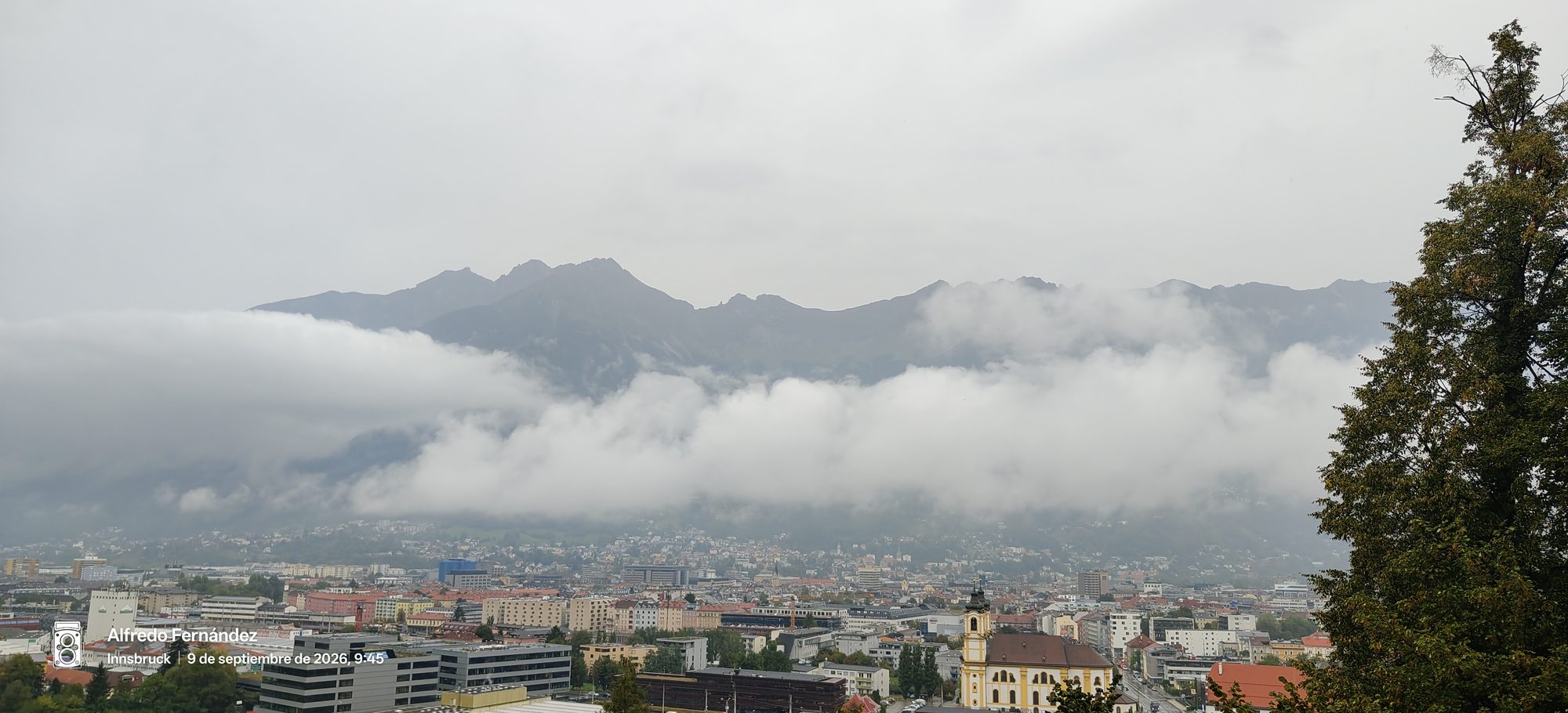 Vista panorámica de Innsbruck con montañas alpinas parcialmente cubiertas por densas nubes bajas.