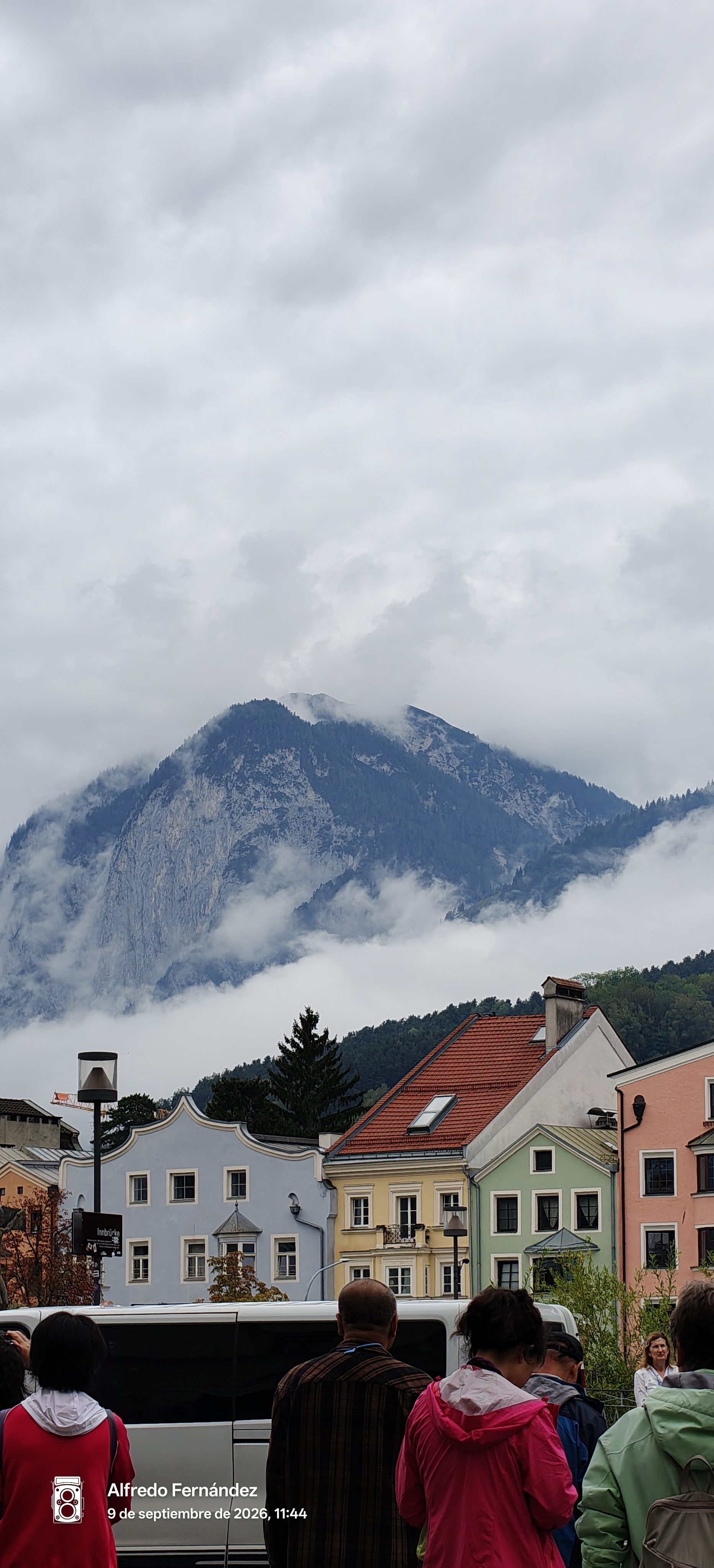 Edificios tradicionales de colores frente a una imponente montaña envuelta en nubes en Innsbruck.