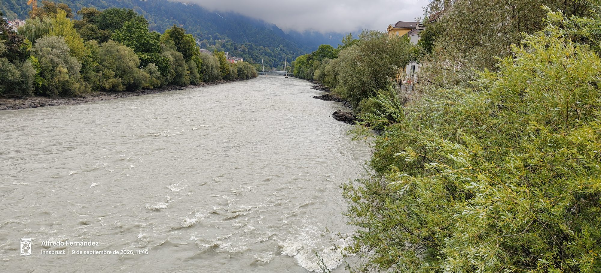 Río Inn fluyendo entre orillas arboladas bajo montañas cubiertas de niebla en Innsbruck.