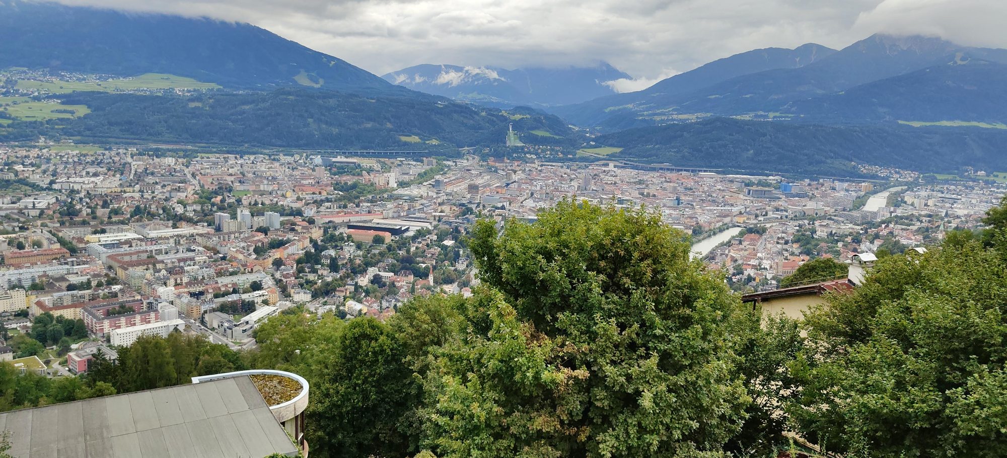 Panorámica de la ciudad de Innsbruck rodeada de montañas verdes bajo un cielo nublado.