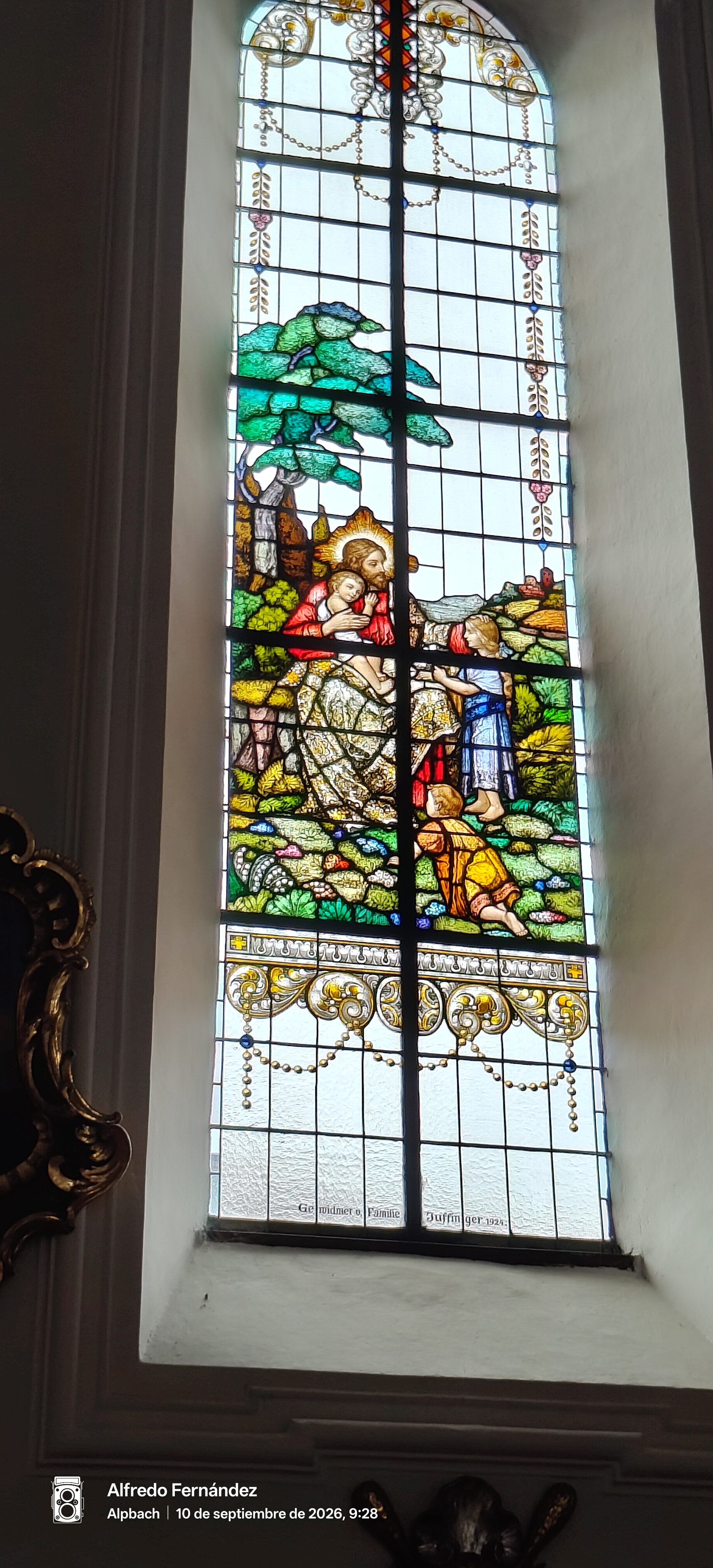 Vidriera policromada en una iglesia con una escena religiosa de Jesús bendiciendo a niños.