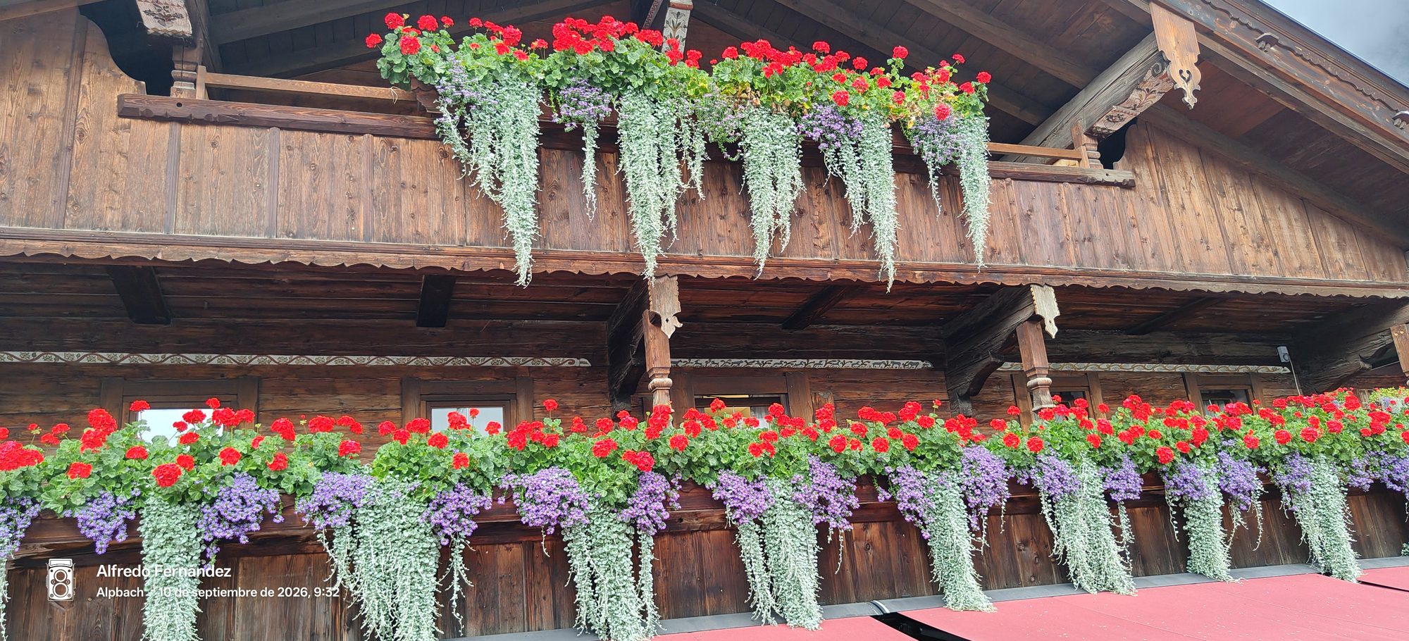 Balcones de madera tradicionales decorados con geranios rojos y plantas colgantes en flor.