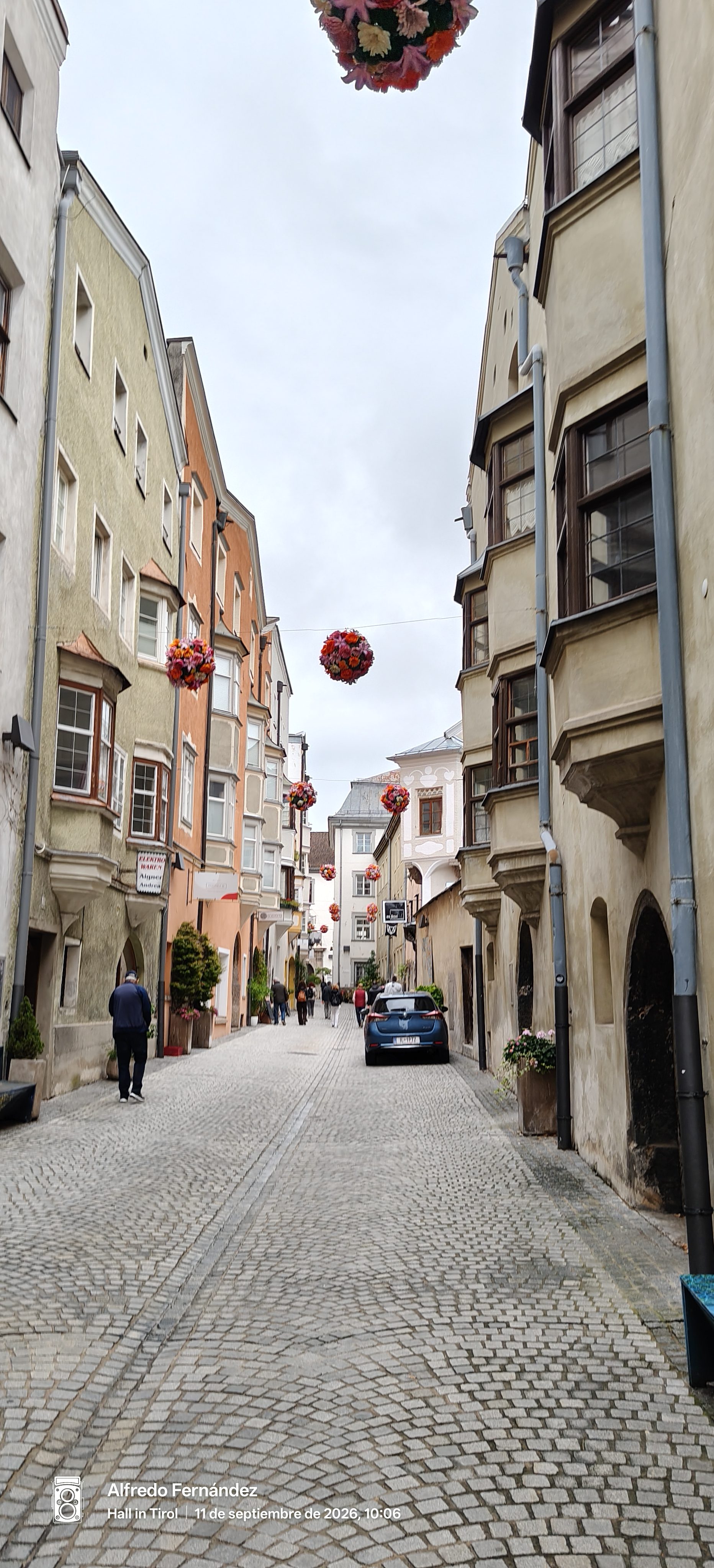 Calle adoquinada con edificios históricos y coloridas esferas de flores suspendidas en el aire.