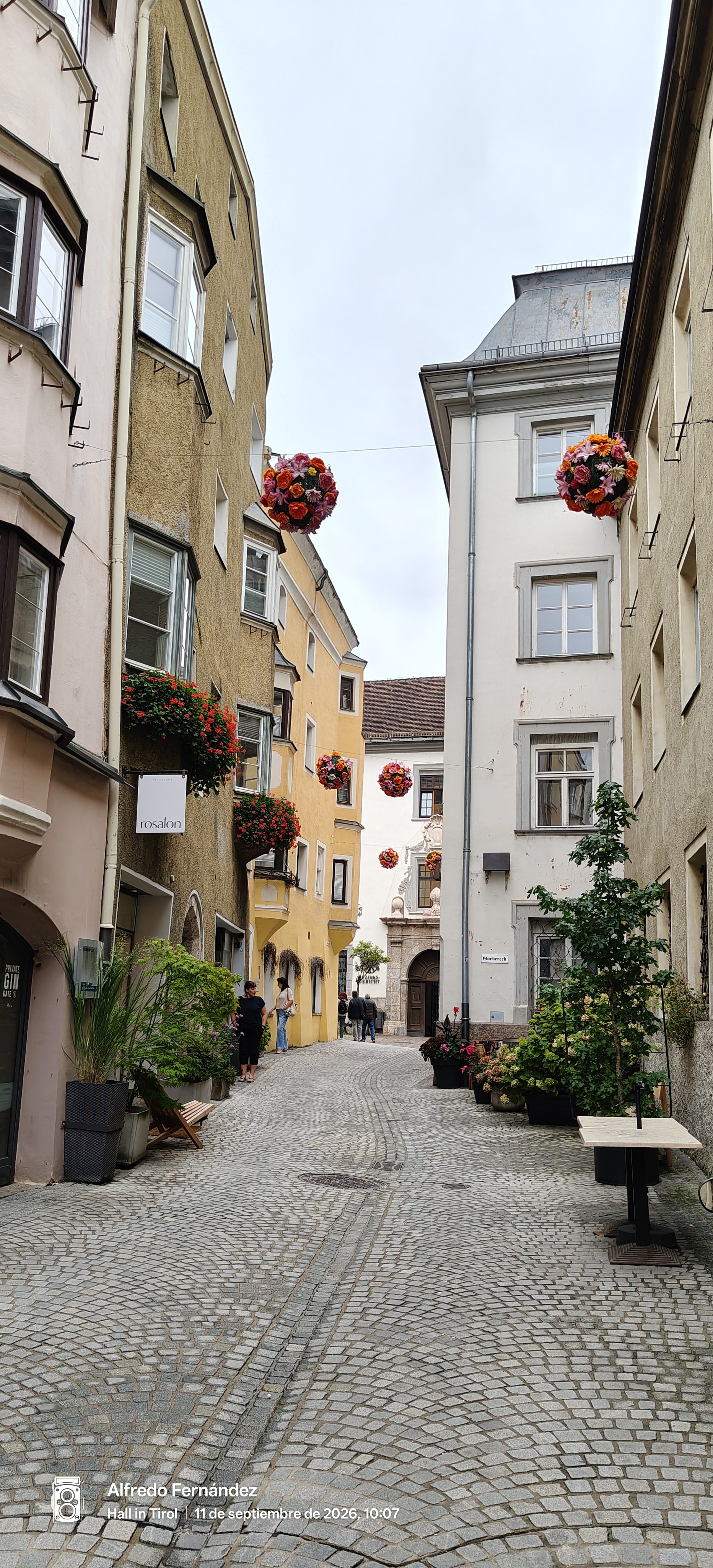 Calle empedrada con edificios tradicionales y esferas de flores suspendidas en Hall in Tirol.