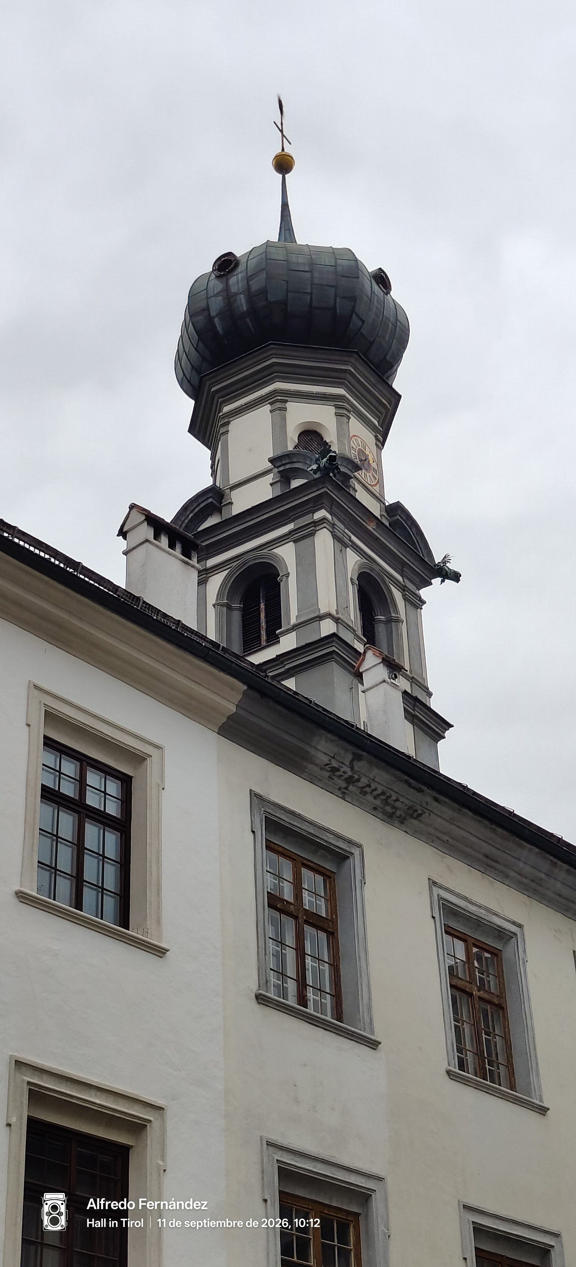 Campanario con cúpula de bulbo y reloj sobre fachada histórica bajo cielo nublado.