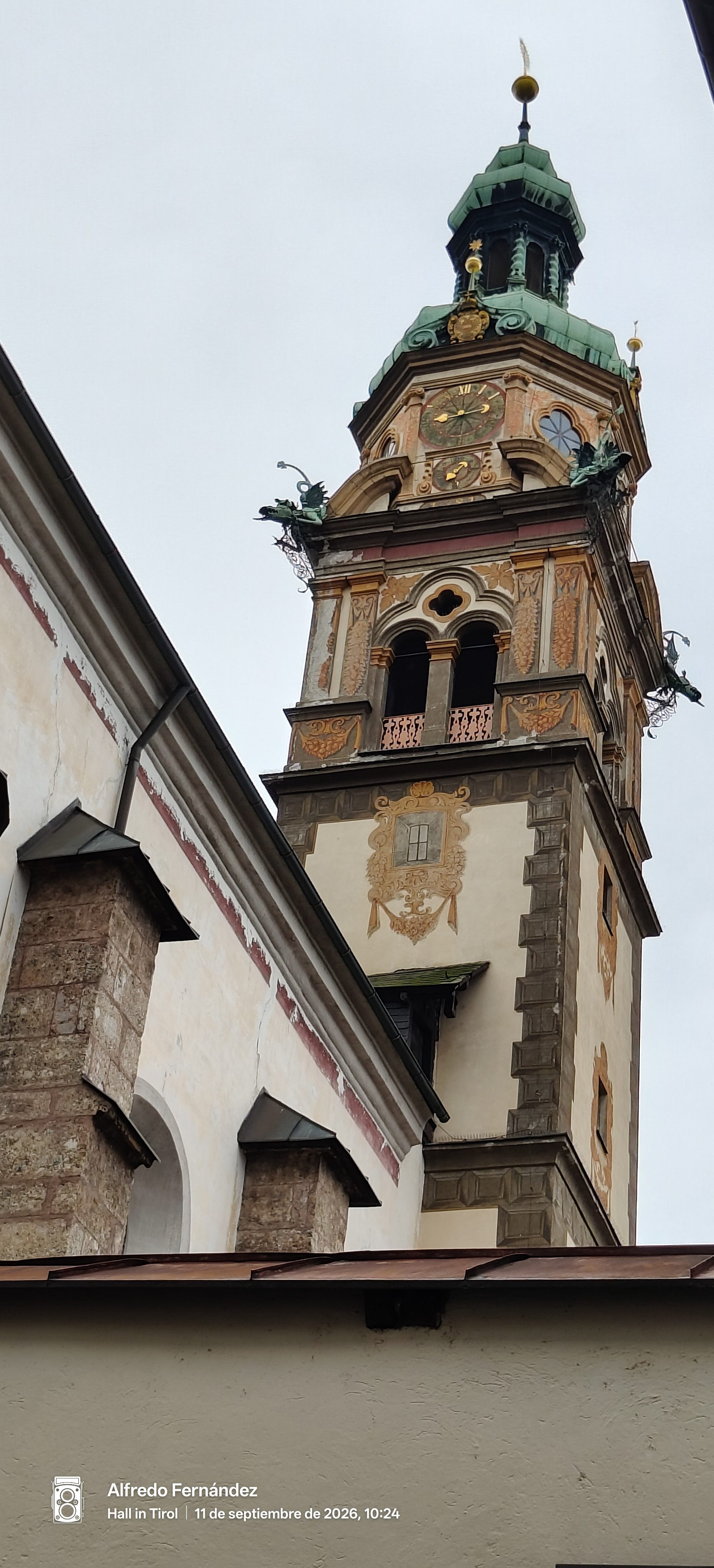 Campanario histórico decorado con pinturas, reloj y cúpula de cobre verde en Hall in Tirol.