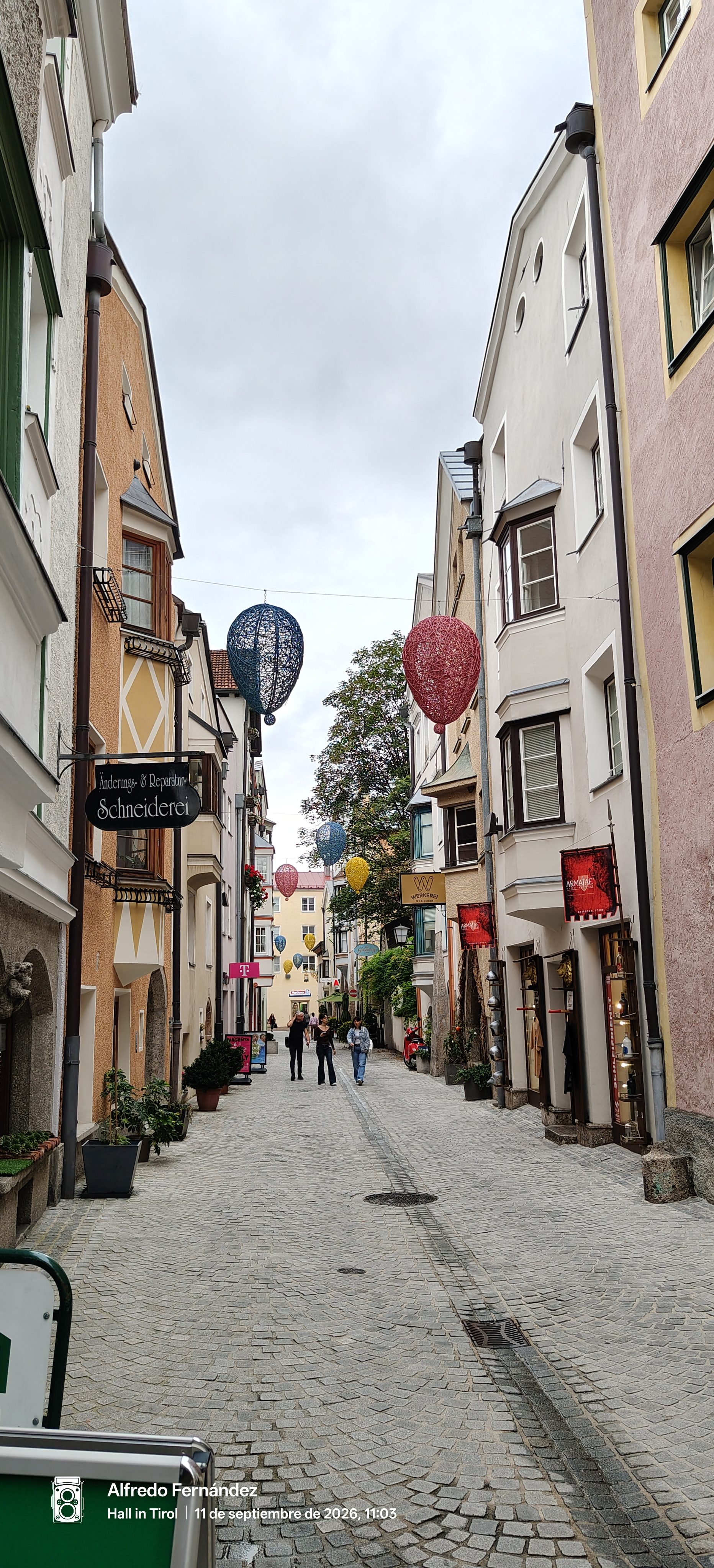 Calle empedrada con edificios históricos y adornos colgantes de colores en Hall in Tirol.