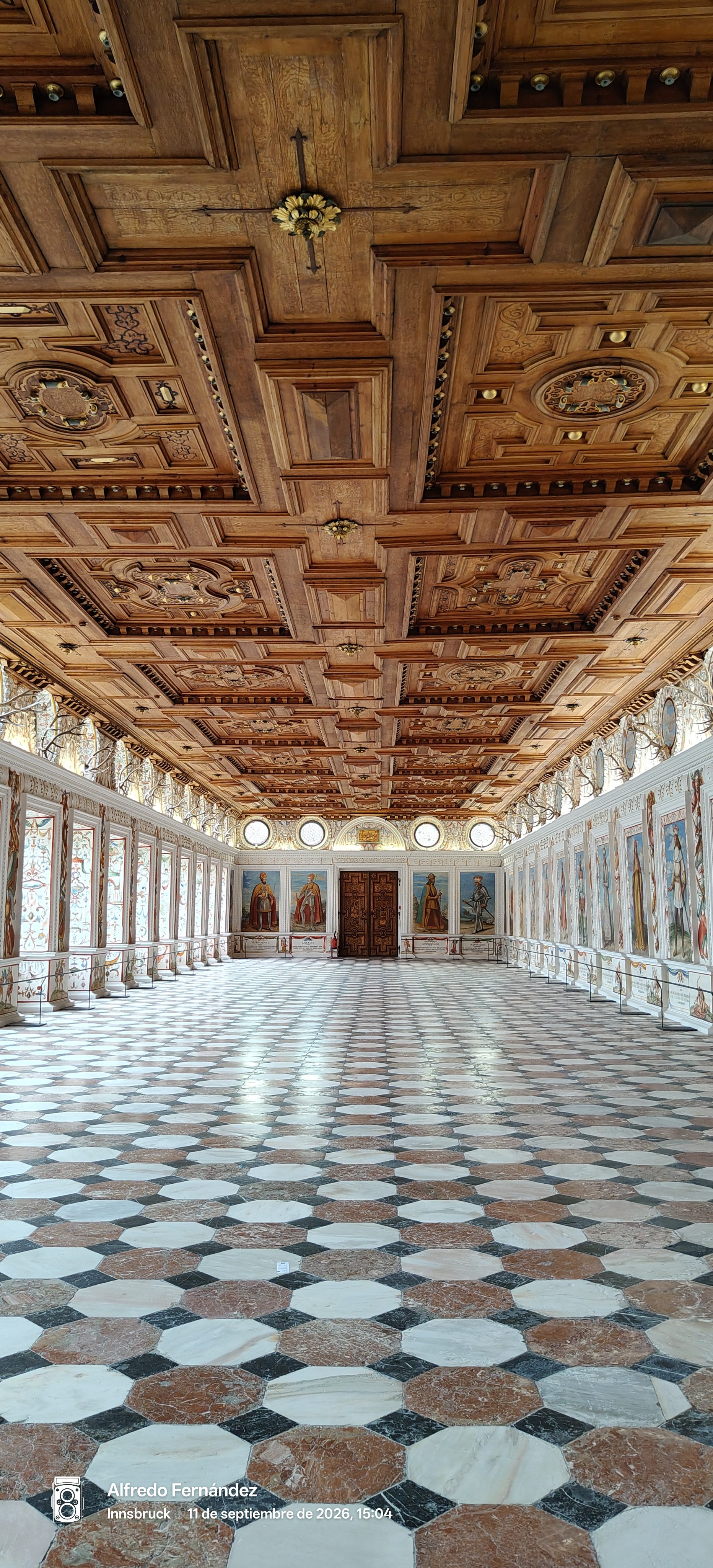 Gran salón renacentista con techo artesonado de madera y suelo geométrico de baldosas.