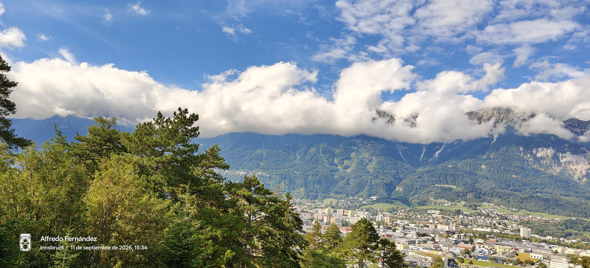 Vista panorámica de Innsbruck y los Alpes austríacos bajo nubes blancas y cielo azul.