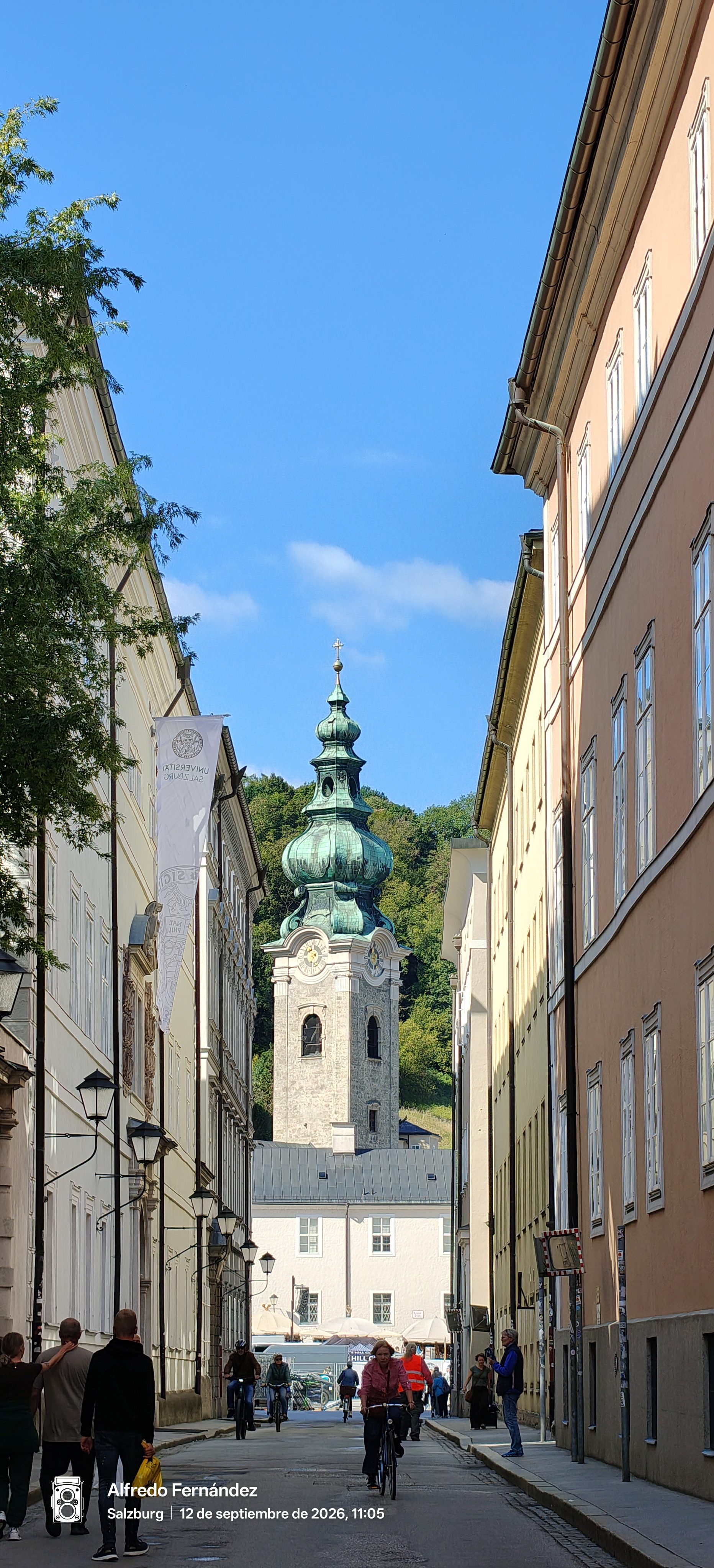Calle estrecha entre edificios históricos con vista a un campanario barroco en Salzburgo.
