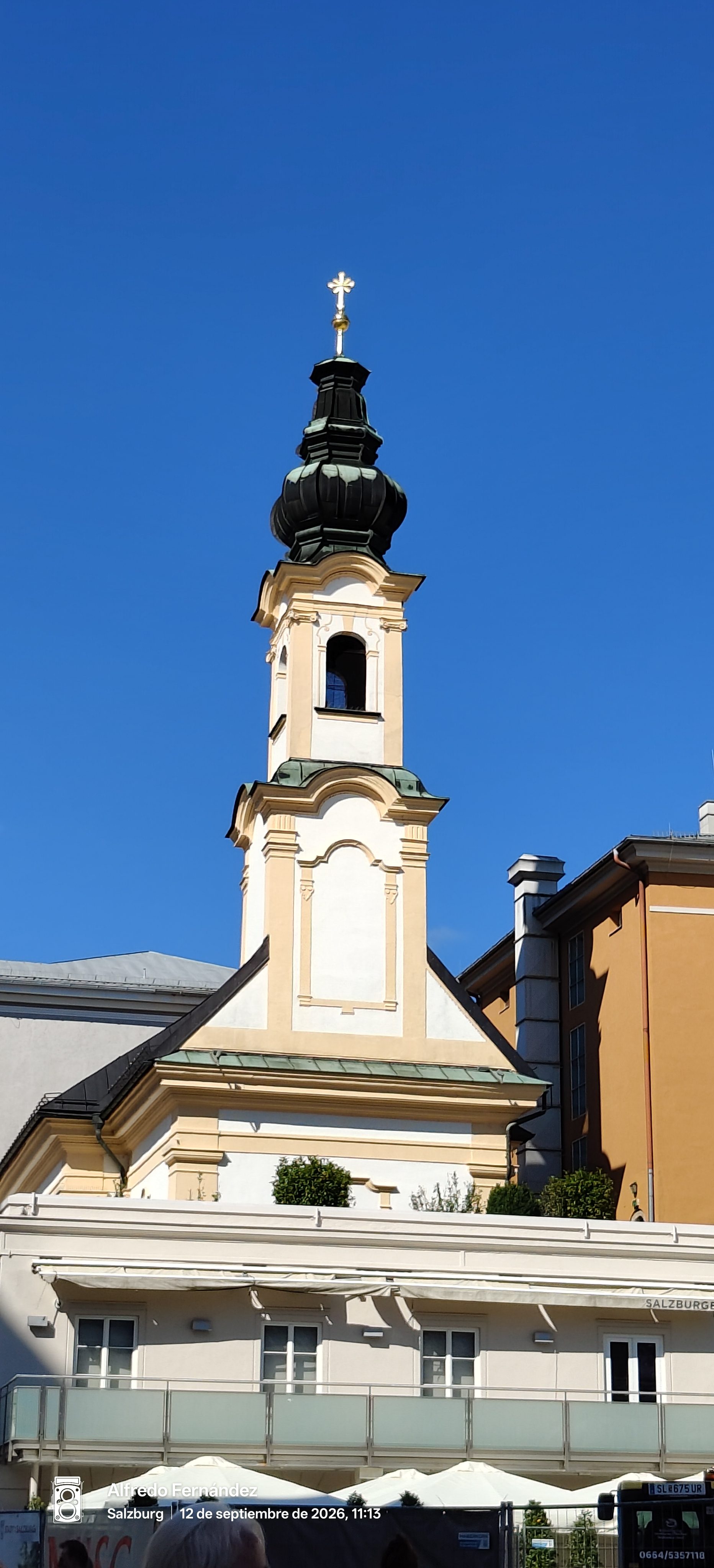 Torre de iglesia barroca con cúpula y cruz dorada bajo un cielo azul despejado.