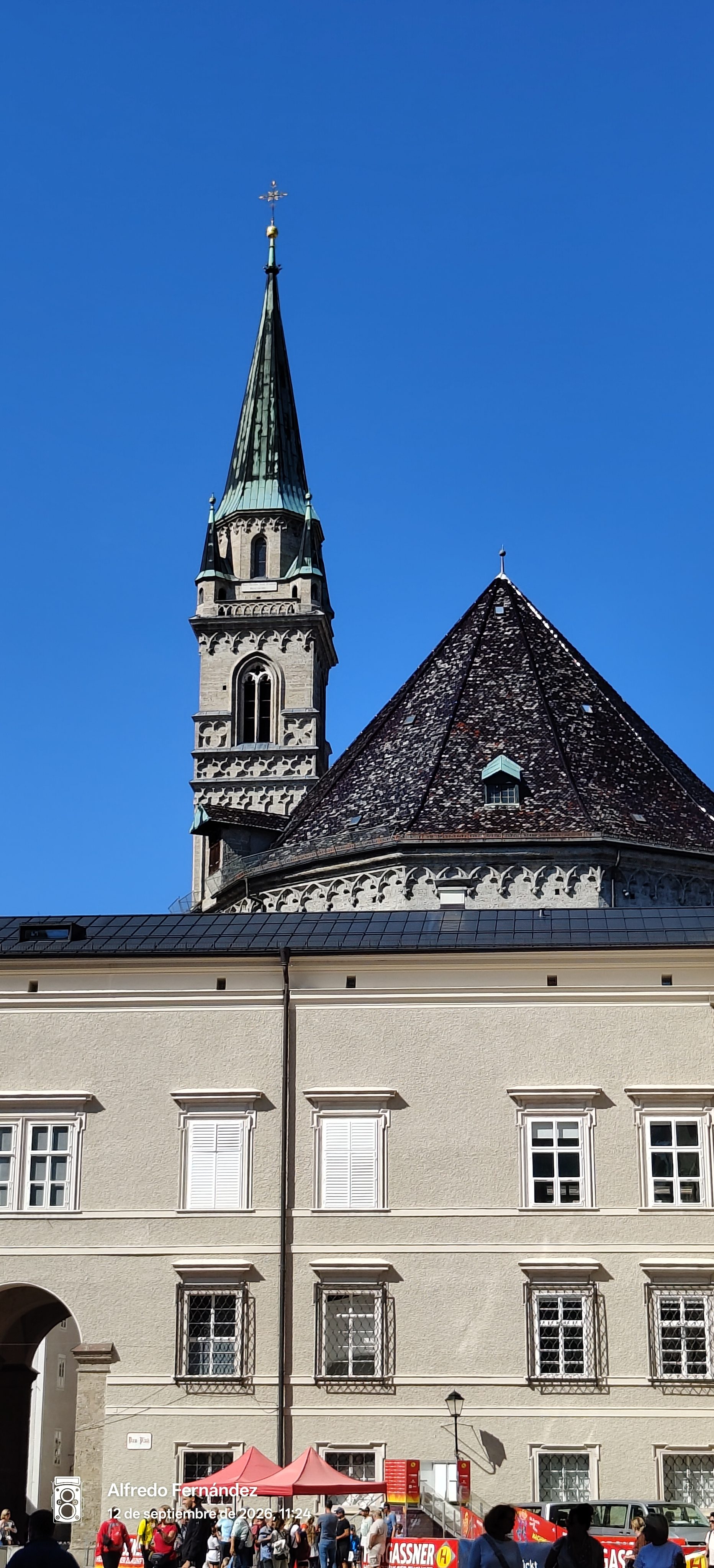 Campanario gótico y tejado cónico de una iglesia sobre un edificio histórico en Salzburgo.