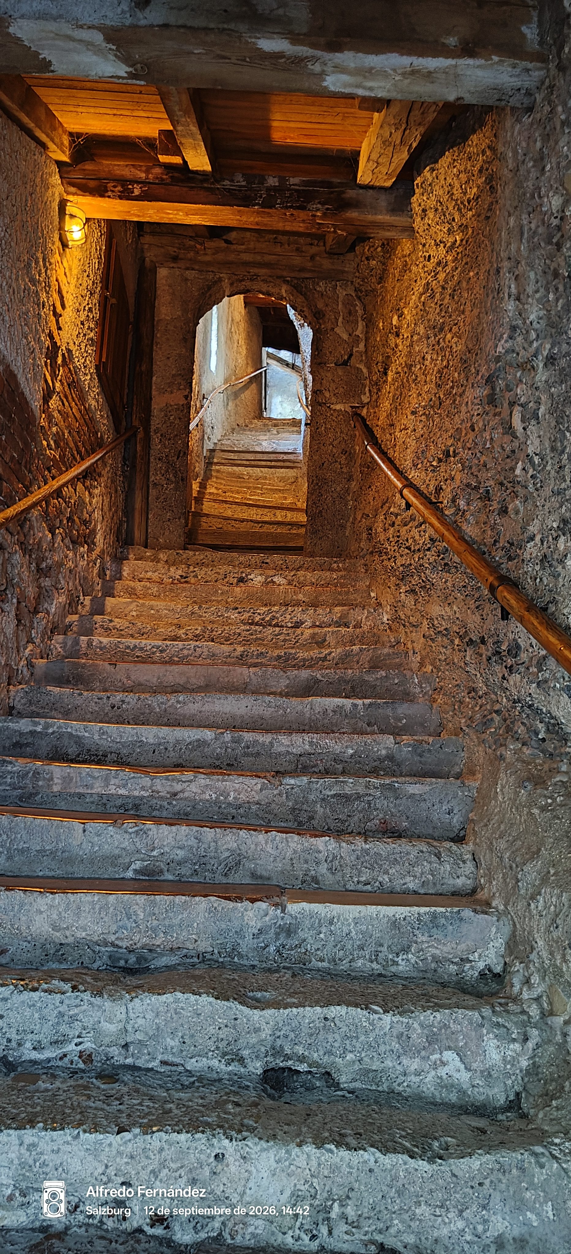 Escalera medieval de piedra iluminada en un estrecho pasaje histórico con vigas de madera.