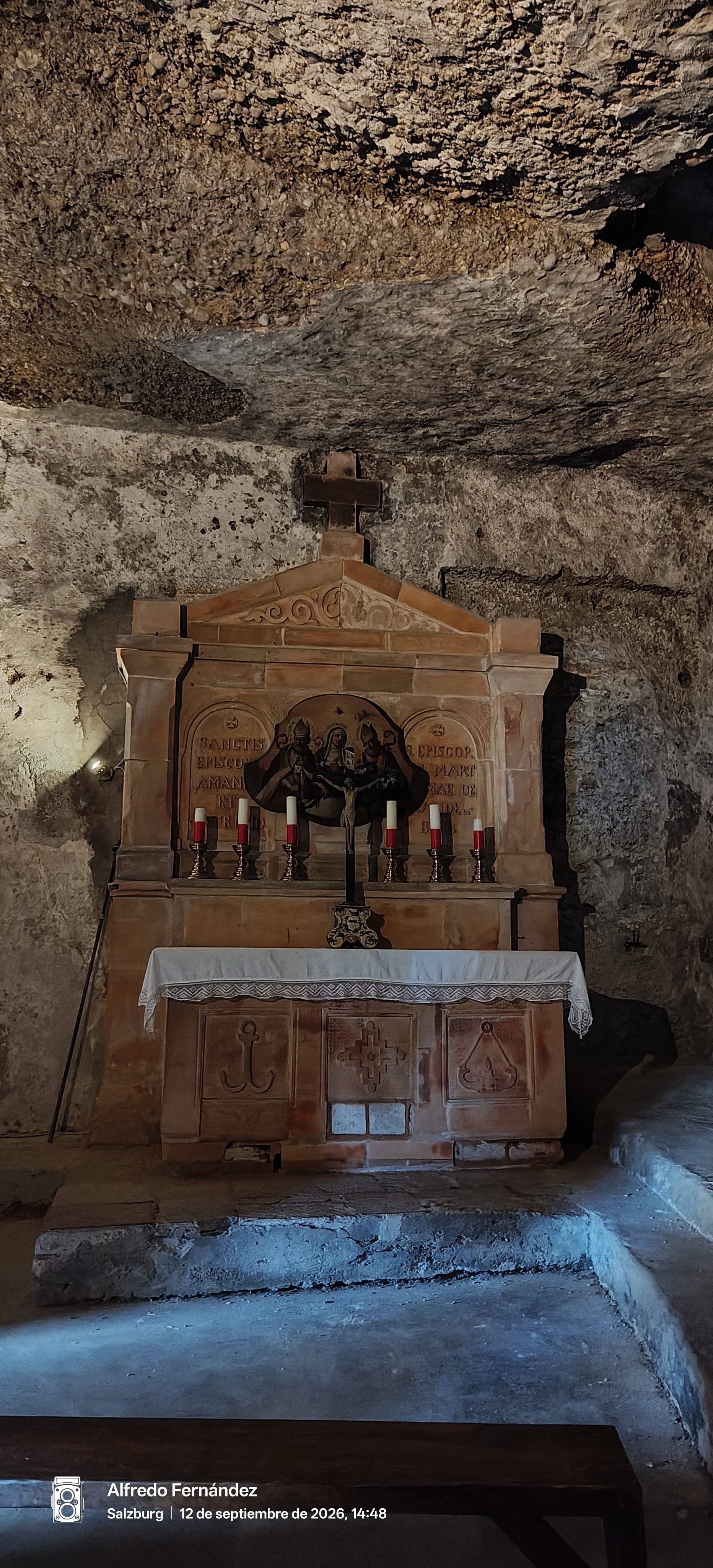 Altar de piedra con velas y crucifijo en una capilla subterránea de roca.