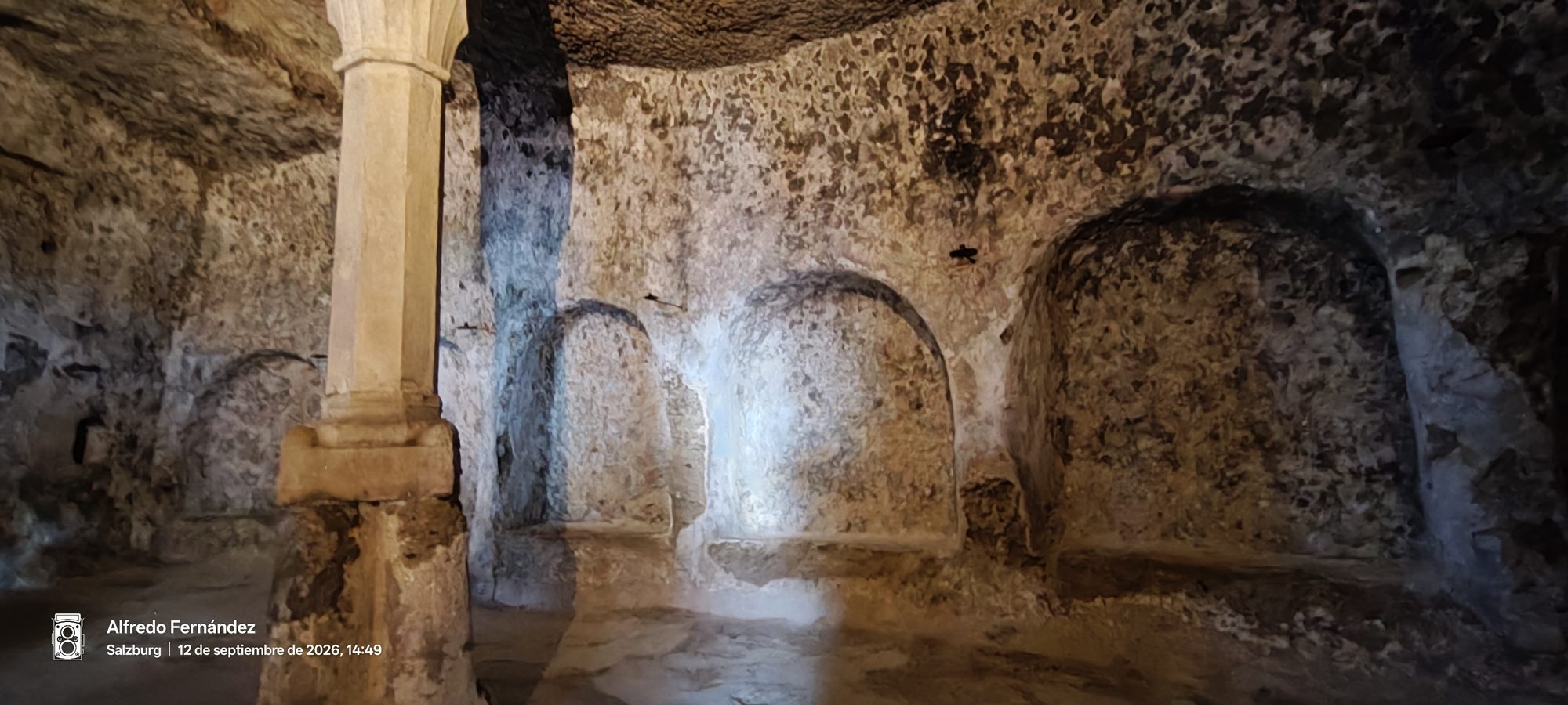 Interior de antiguas catacumbas talladas en la roca con nichos arqueados y una columna.