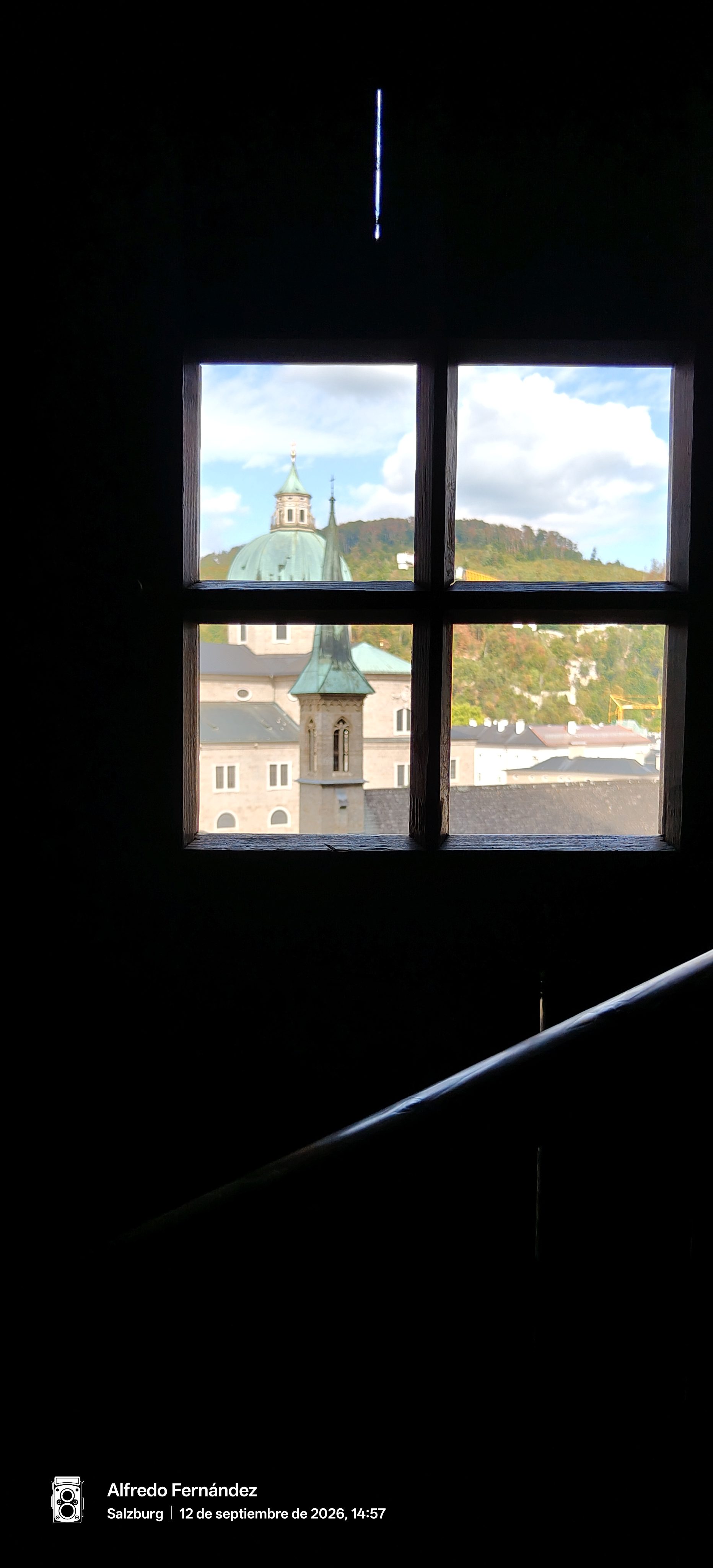 Cúpulas históricas y colinas de Salzburgo enmarcadas a través de una ventana de madera oscura.