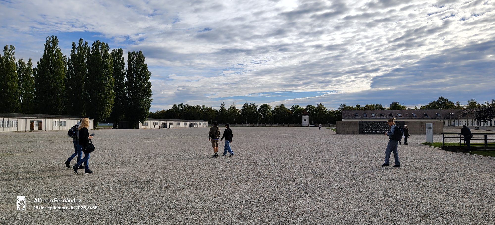 Patio central de grava del memorial de Dachau con edificios históricos y visitantes bajo cielo nublado.