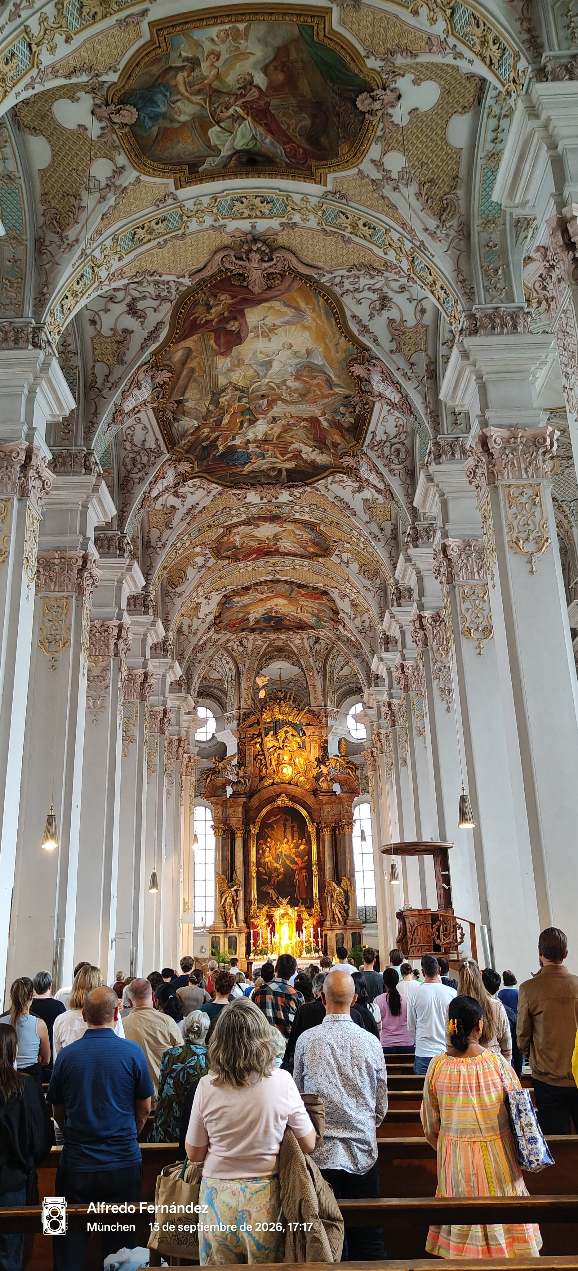 Interior de una iglesia barroca con frescos en el techo y un altar dorado iluminado.
