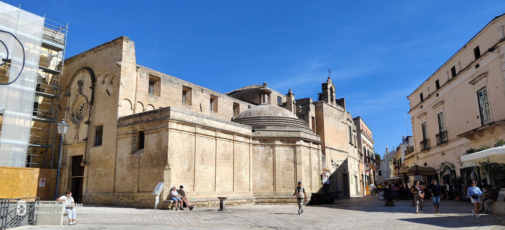 Iglesia románica de piedra y plaza soleada con transeúntes en Matera.