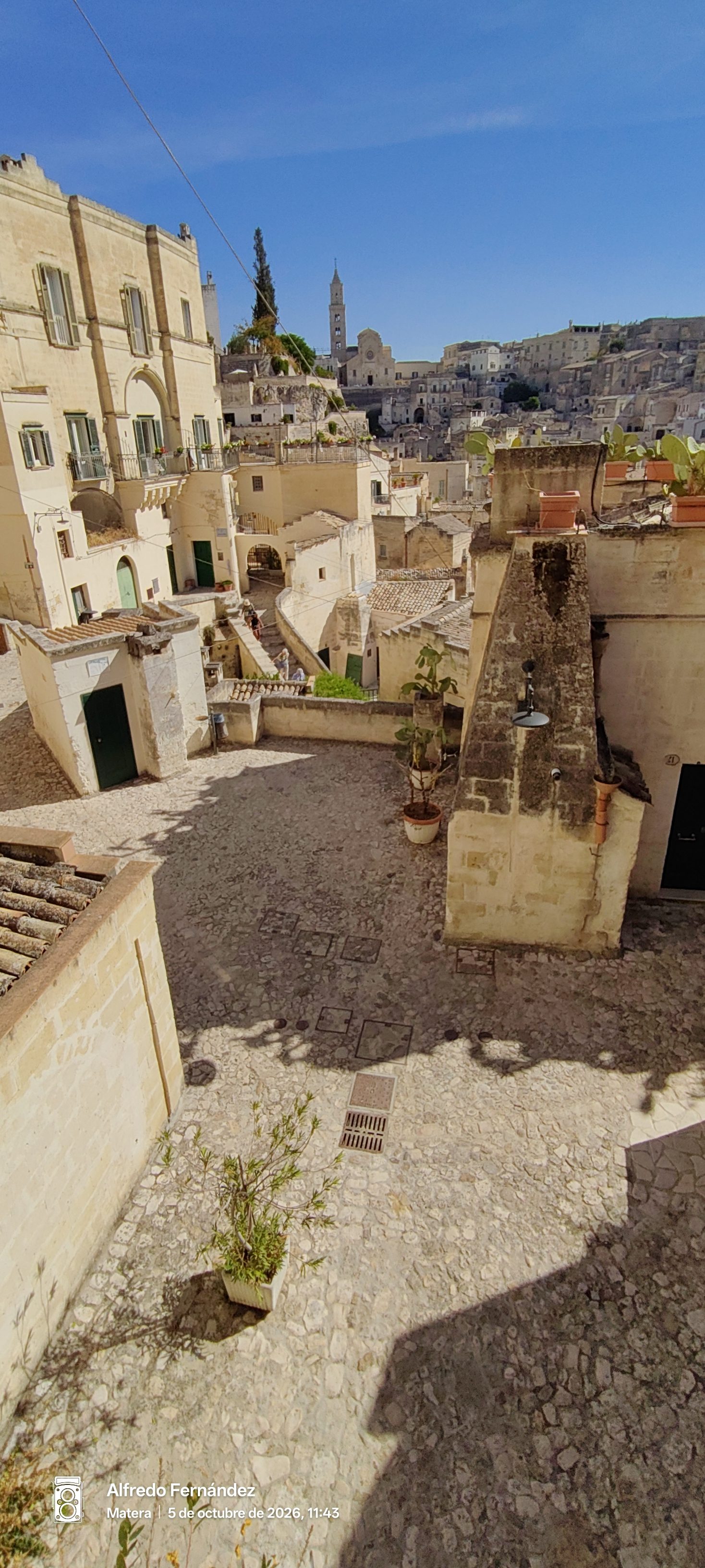 Calles empedradas y casas tradicionales de piedra con un campanario al fondo en Matera.