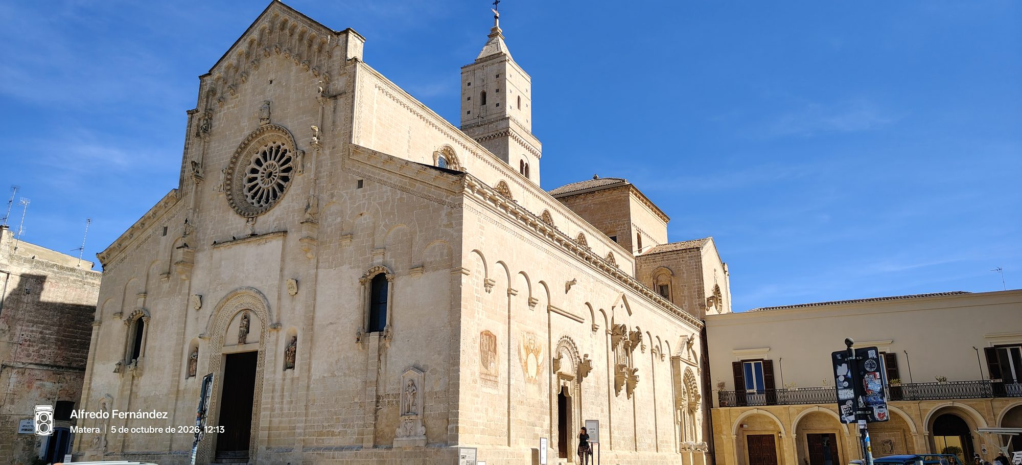 Fachada románica de la Catedral de Matera con rosetón y campanario bajo cielo azul.