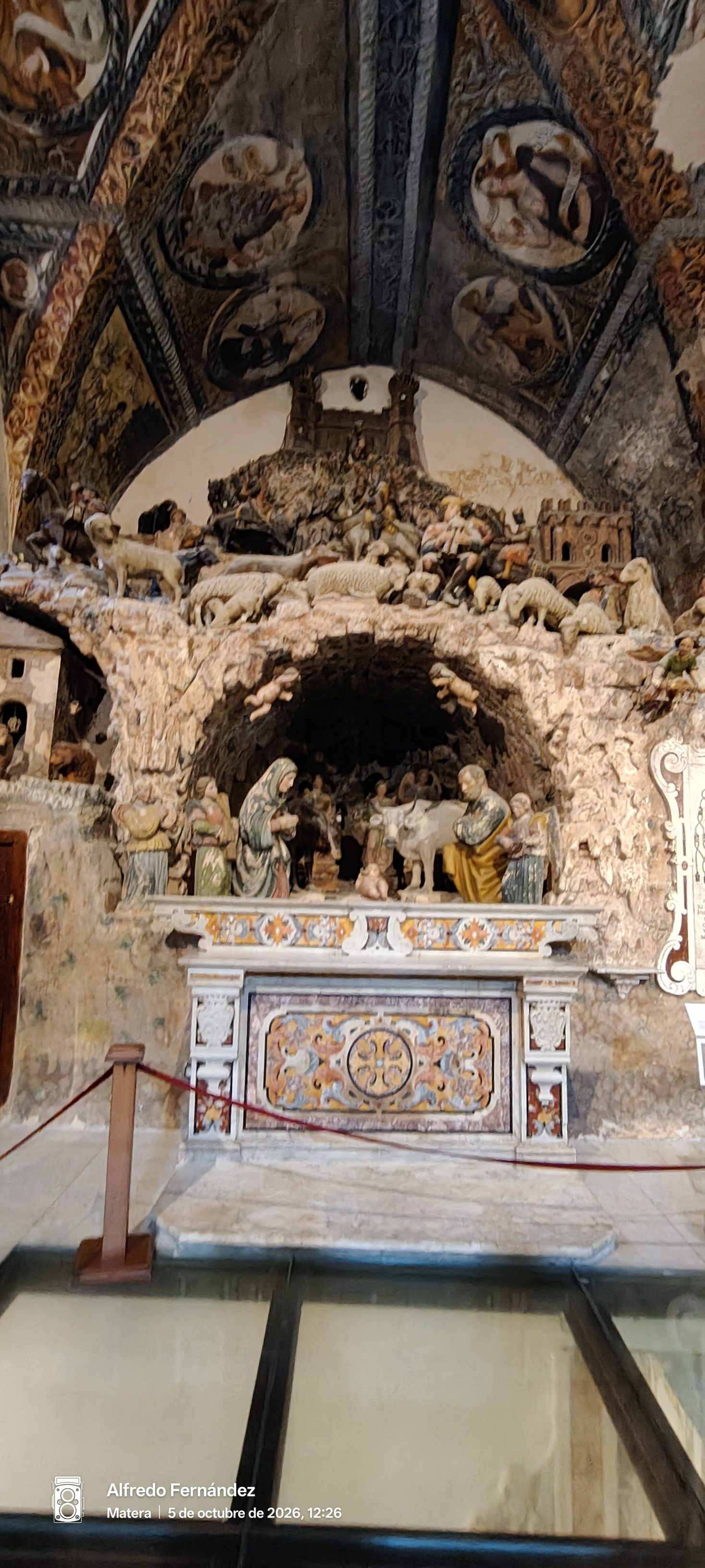 Antiguo belén esculpido en piedra bajo techos con frescos dentro de una iglesia.