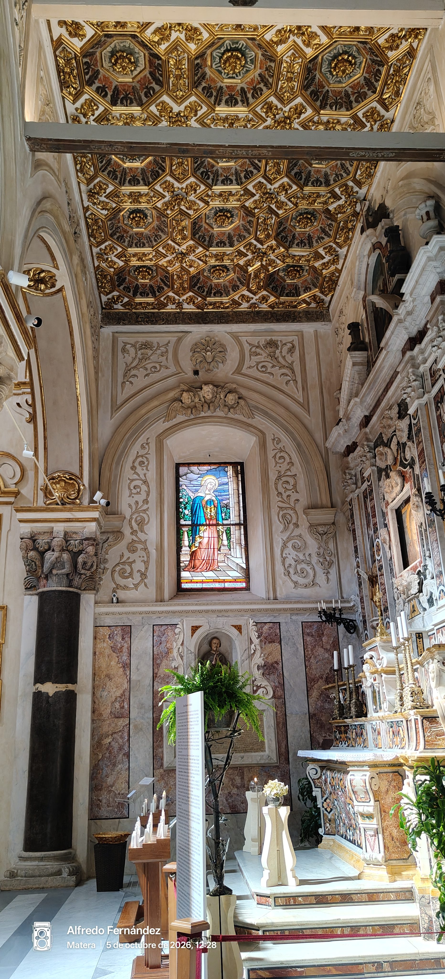 Interior de iglesia con artesonado dorado, vidriera colorida y altar de mármol tallado.