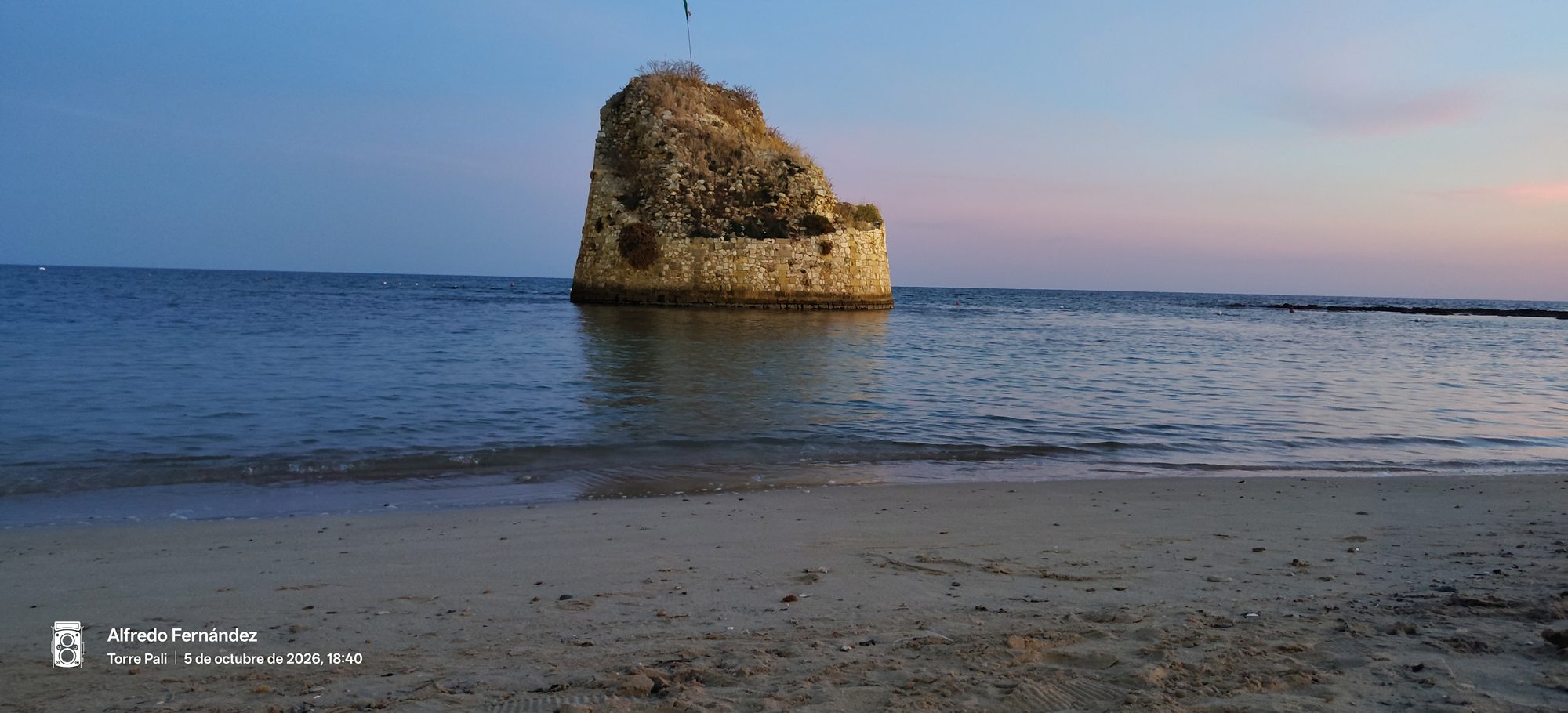 Antigua torre de piedra dentro del mar al atardecer frente a la playa.