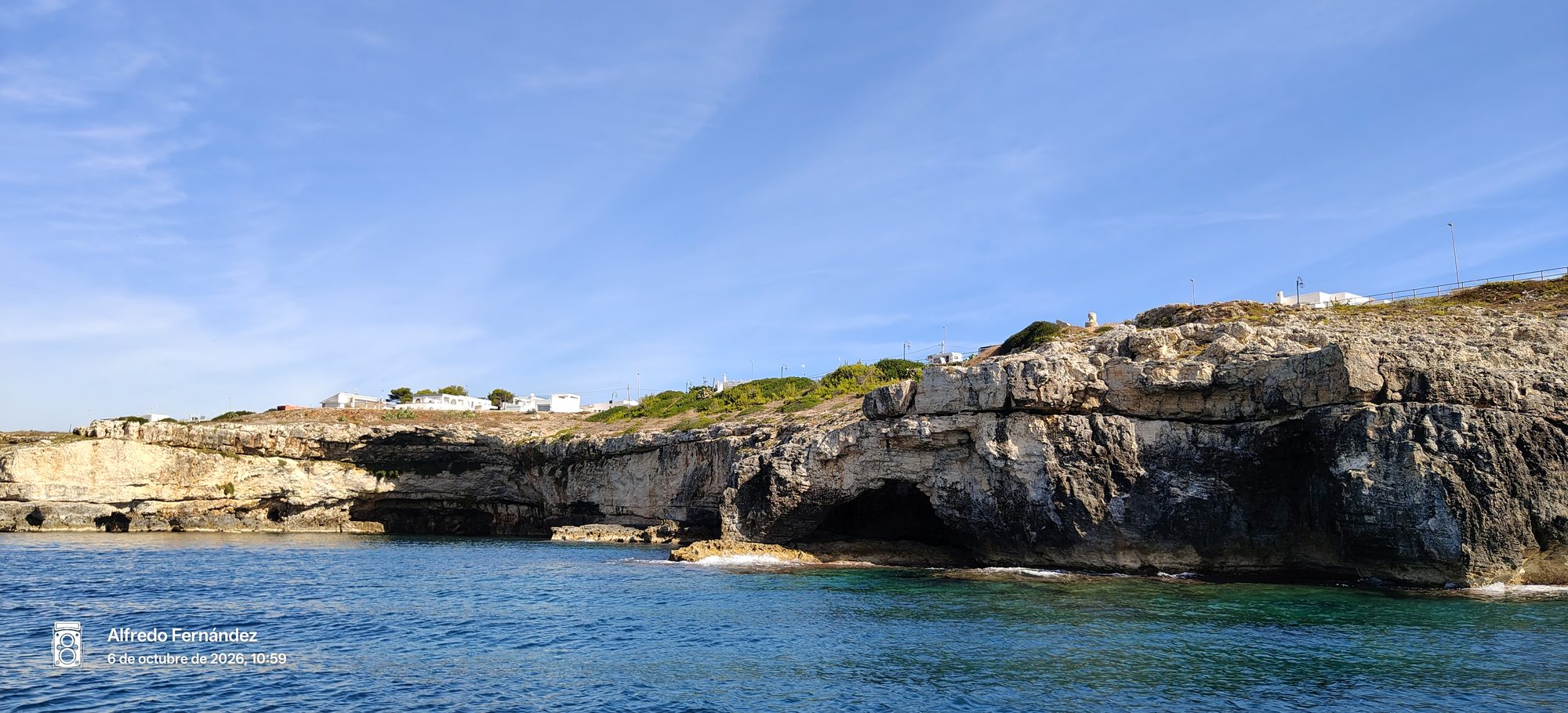 Acantilados rocosos con cuevas marinas sobre aguas turquesas bajo un cielo despejado.