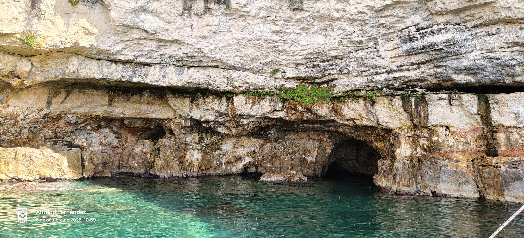 Acantilado rocoso con cuevas marinas sobre aguas cristalinas y turquesas del mar.