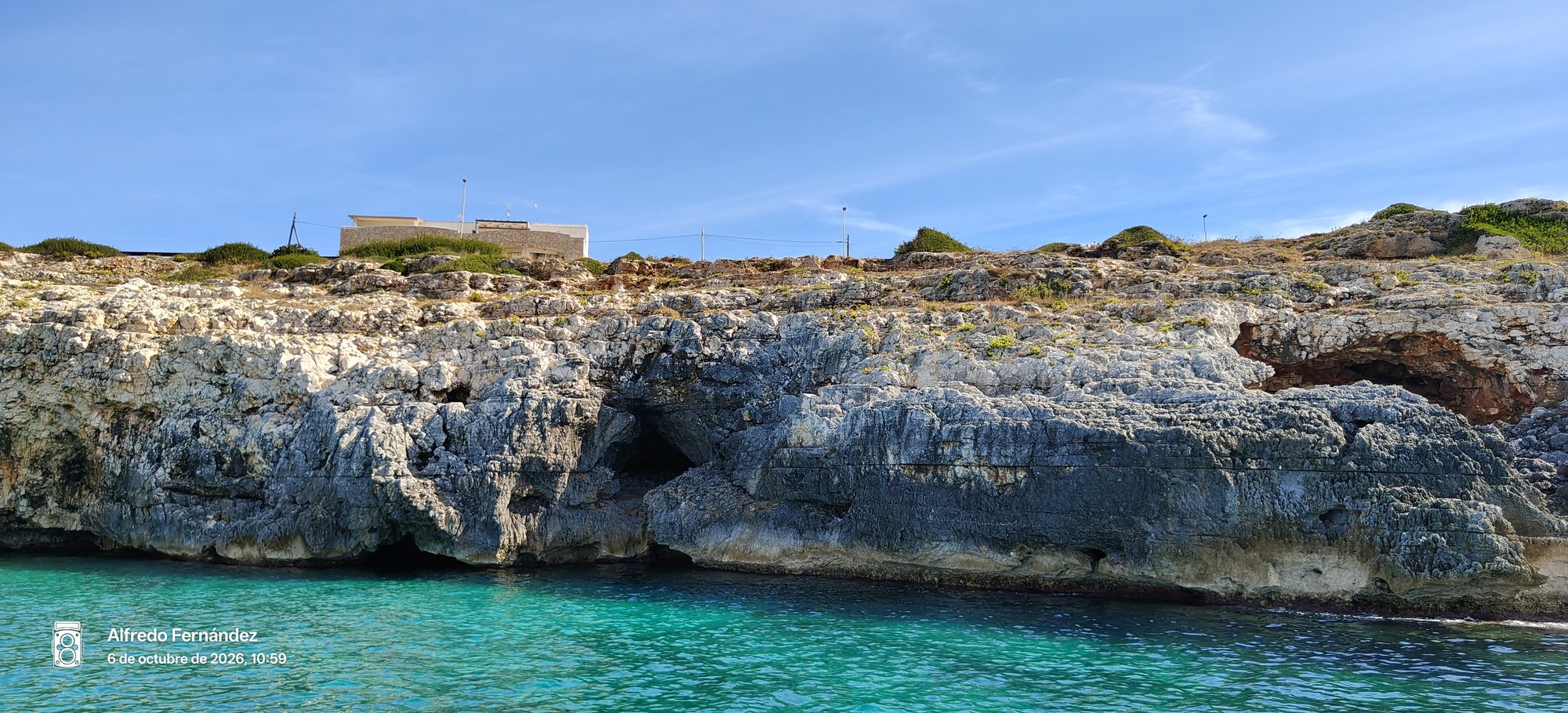 Acantilados rocosos y cuevas marinas frente a aguas turquesas bajo el cielo azul.