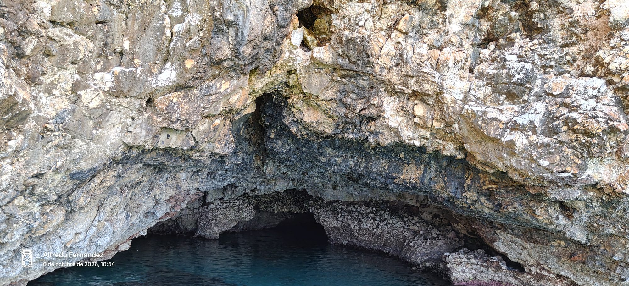 Entrada a una cueva marina de roca escarpada con aguas cristalinas y profundas.
