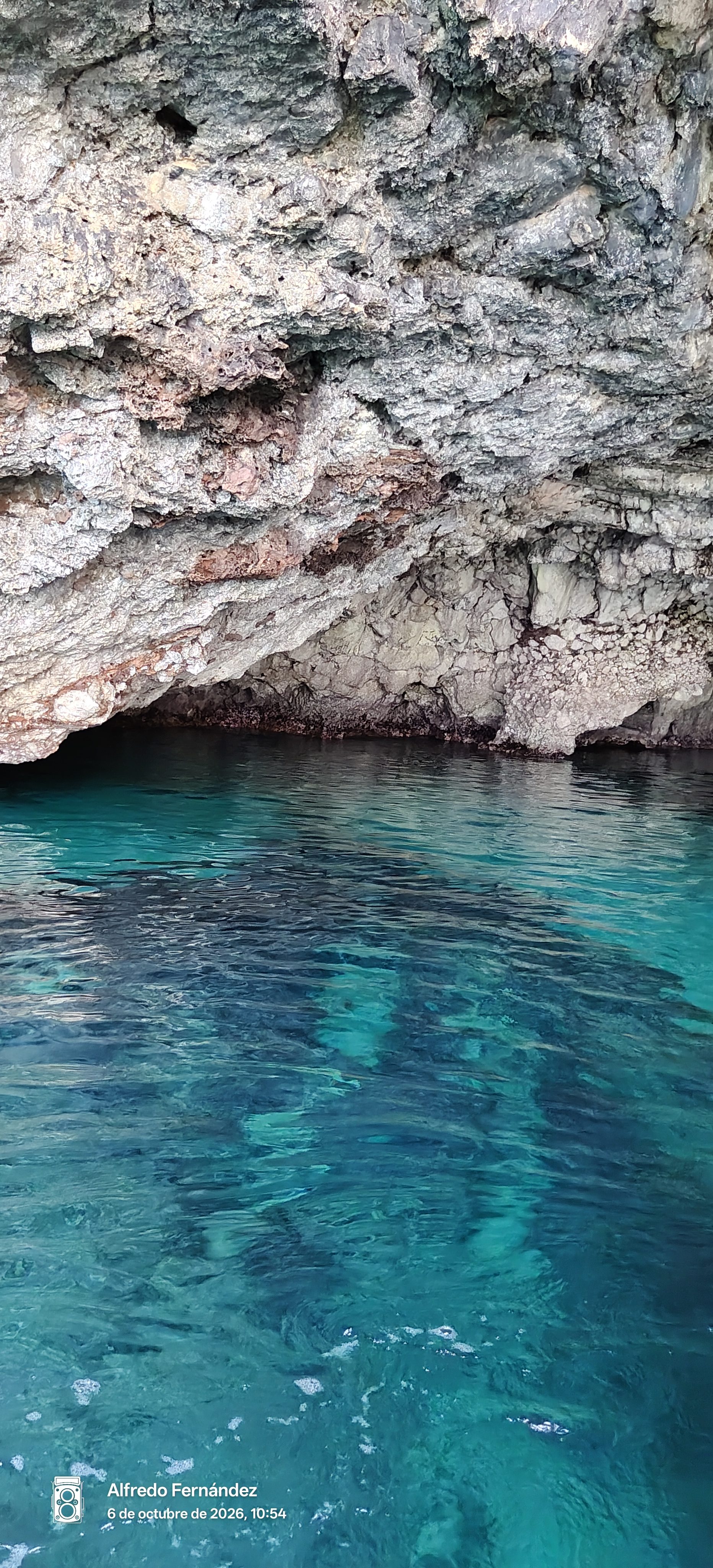 Aguas cristalinas de color turquesa junto a las rocas de una cueva marina.
