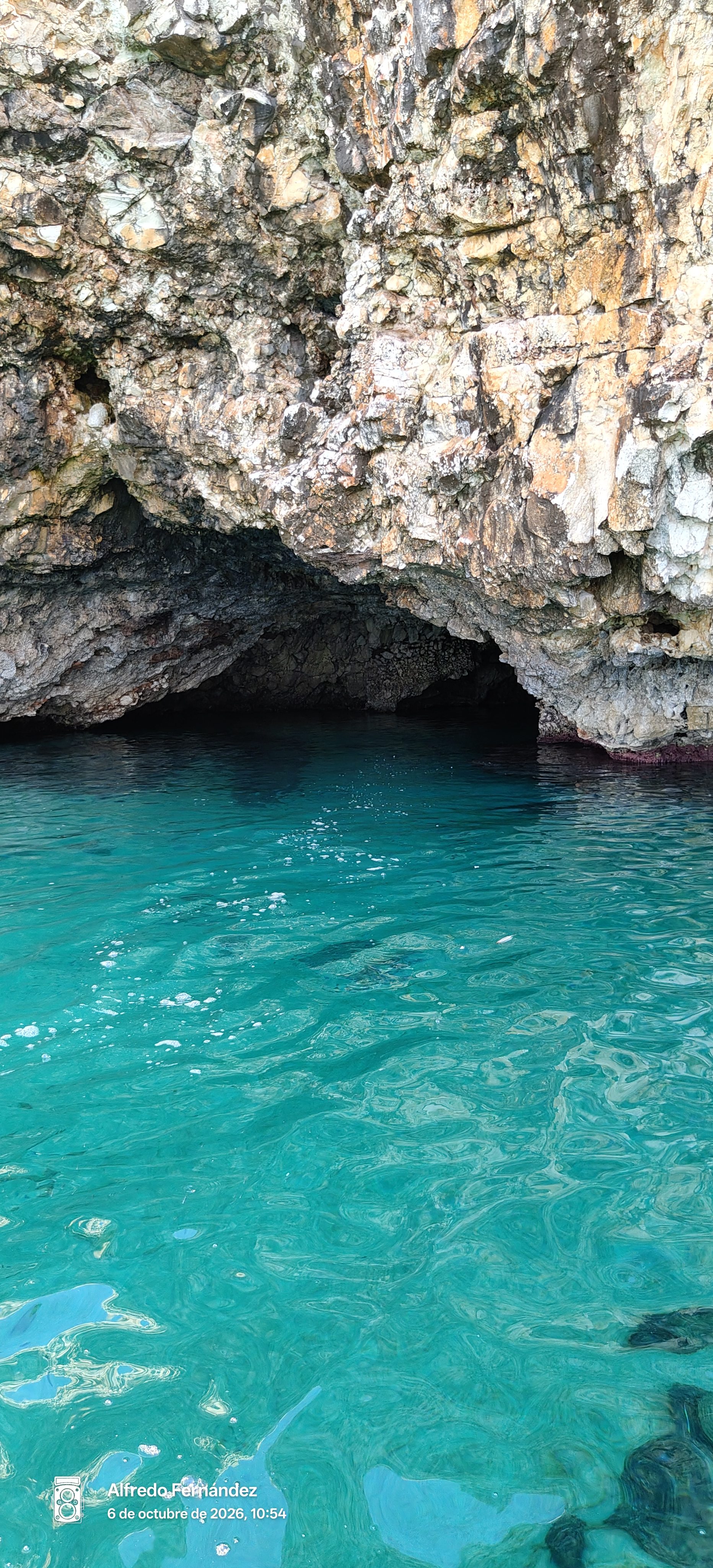 Entrada a una cueva marina con aguas cristalinas de color turquesa bajo acantilados escarpados.