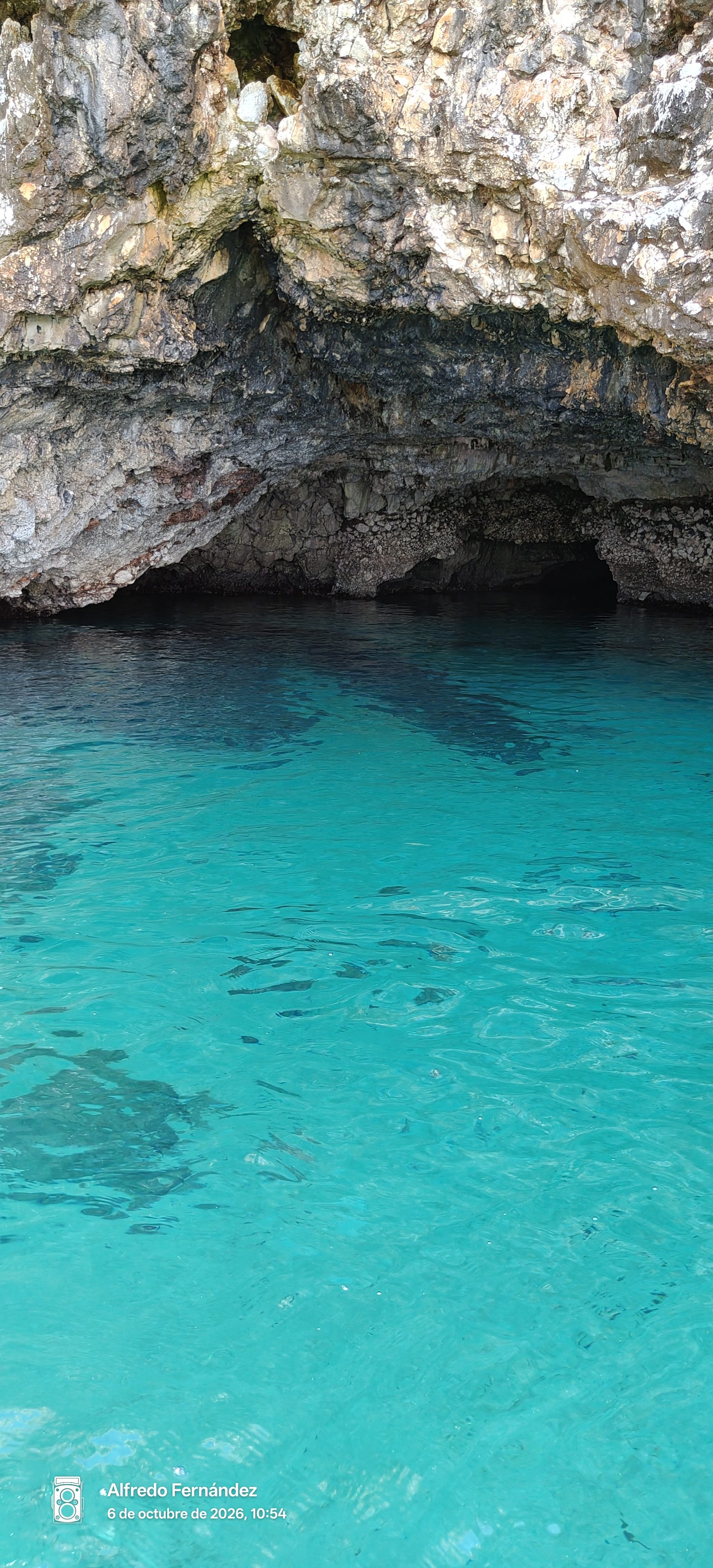 Cueva marina rocosa sobre aguas cristalinas de color turquesa intenso.