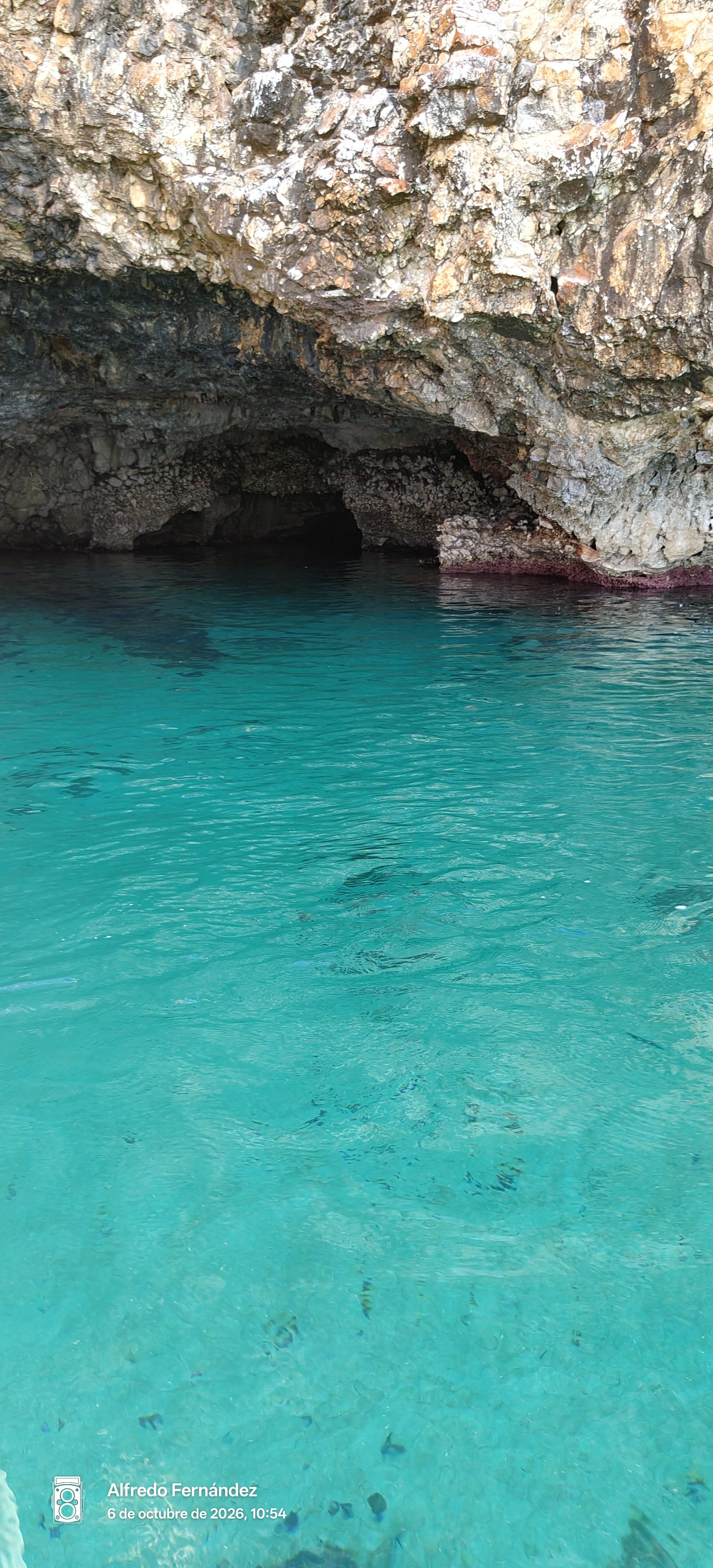 Aguas cristalinas de color turquesa frente a la entrada de una cueva marina rocosa.