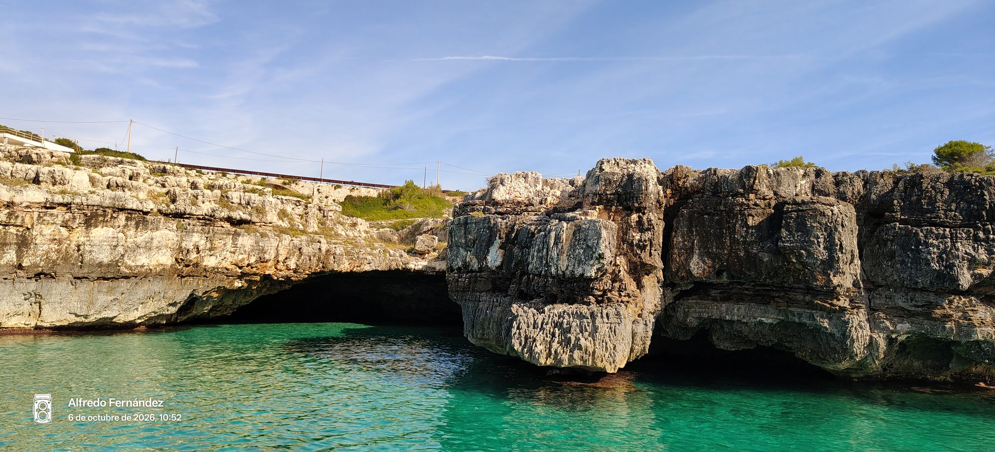 Acantilados rocosos y cuevas marinas frente a aguas turquesas bajo el cielo azul.