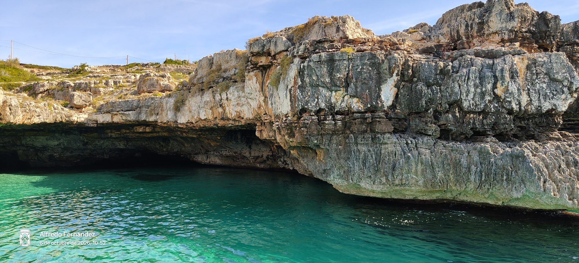 Acantilados rocosos y cueva marina sobre aguas turquesas y cristalinas bajo el sol.
